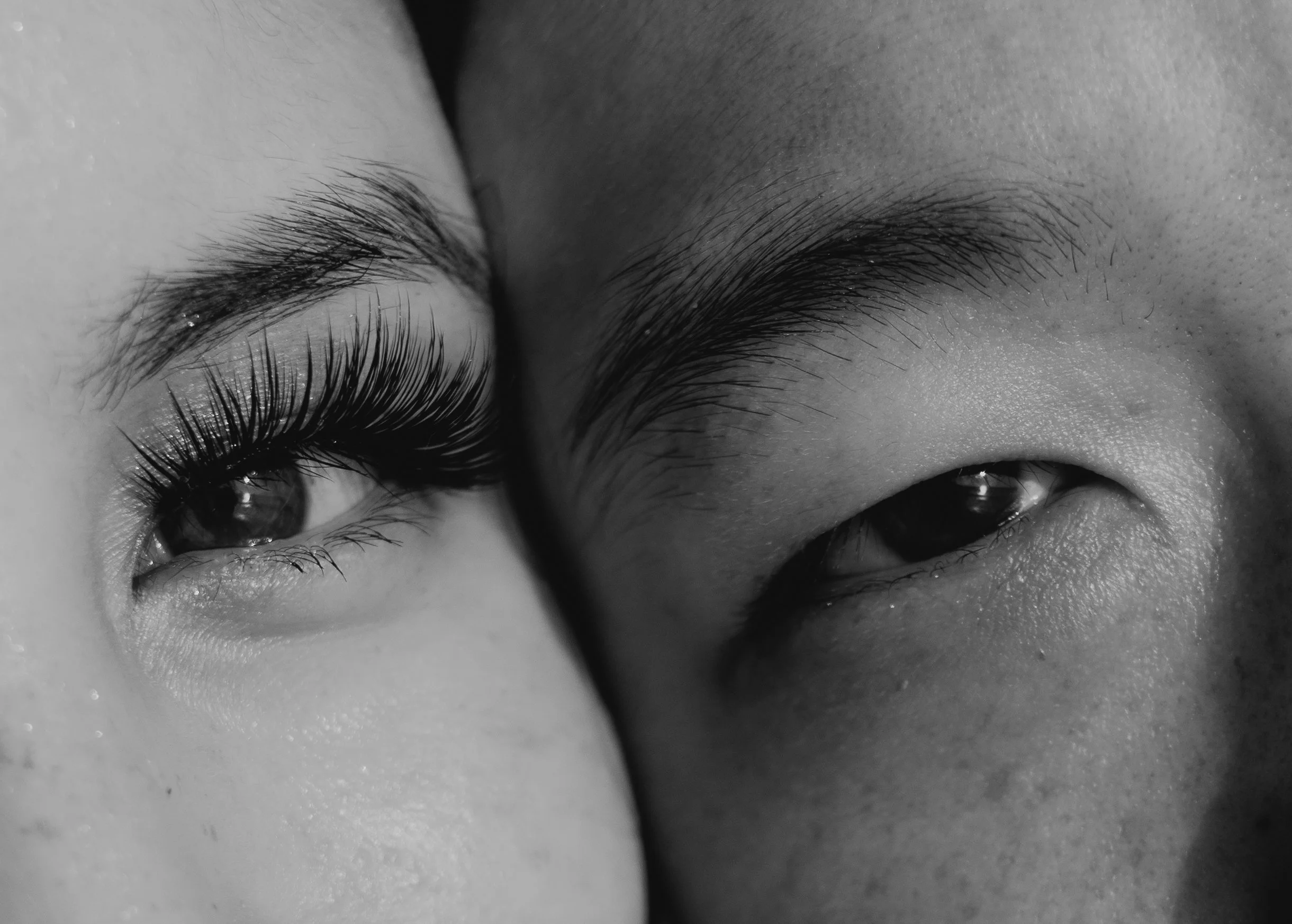 Close-up black and white photograph of a person's closed eyes, showing detailed eyelashes and eyebrows.