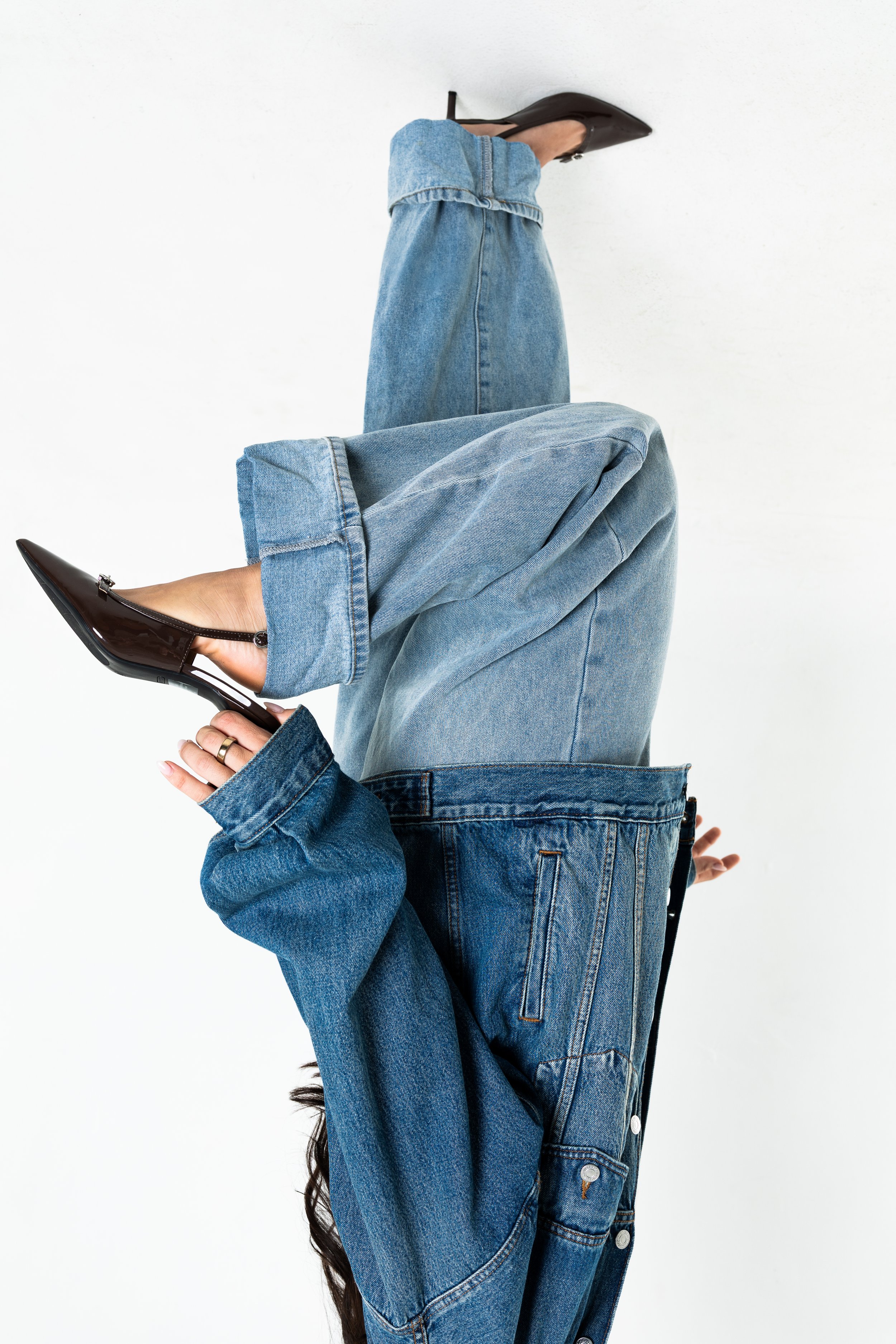 A woman wearing blue jeans, a denim jacket, and black pointed-toe shoes, holding a smartphone, with her long dark hair visible.