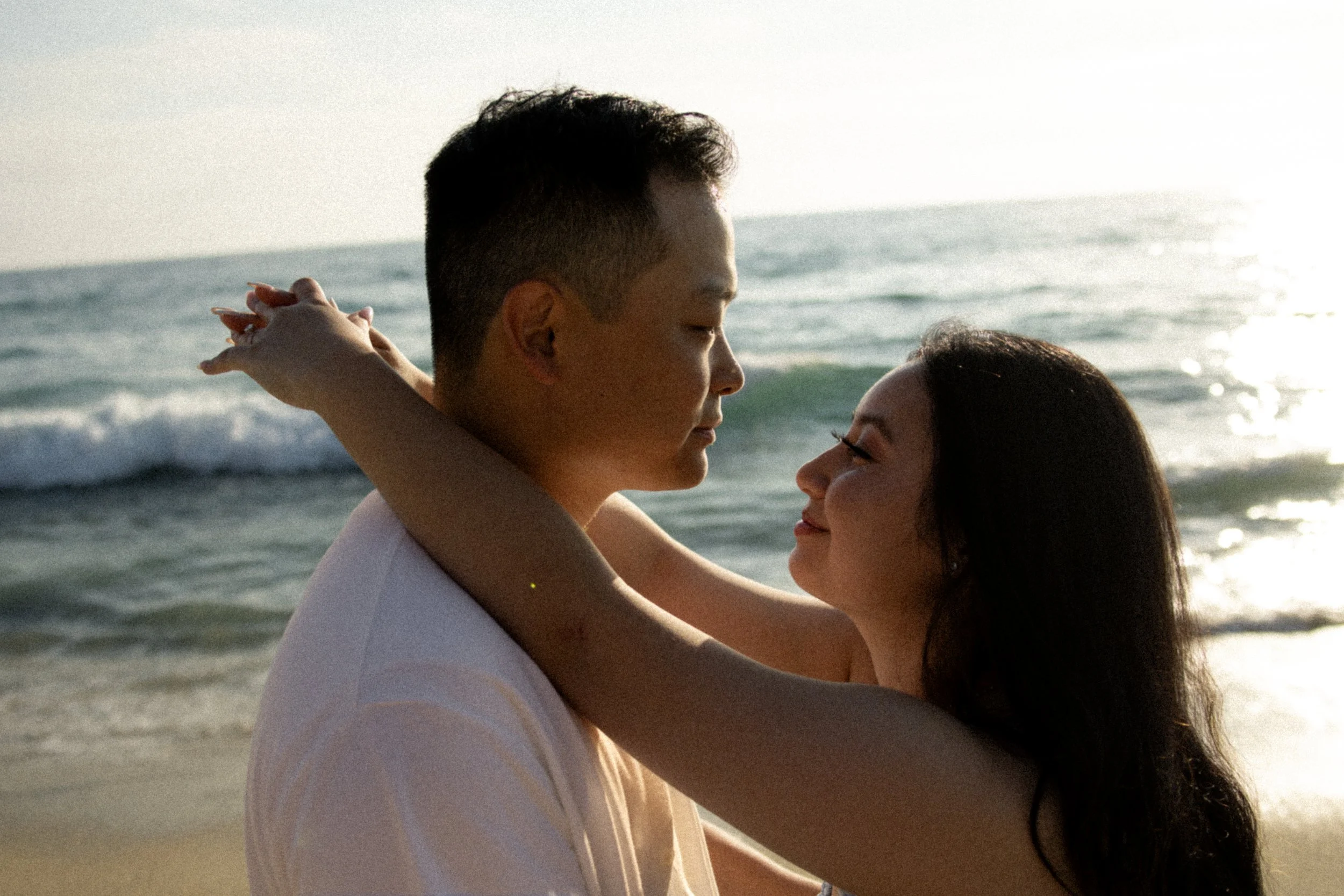 A couple embracing on the beach at sunset, with the ocean in the background.