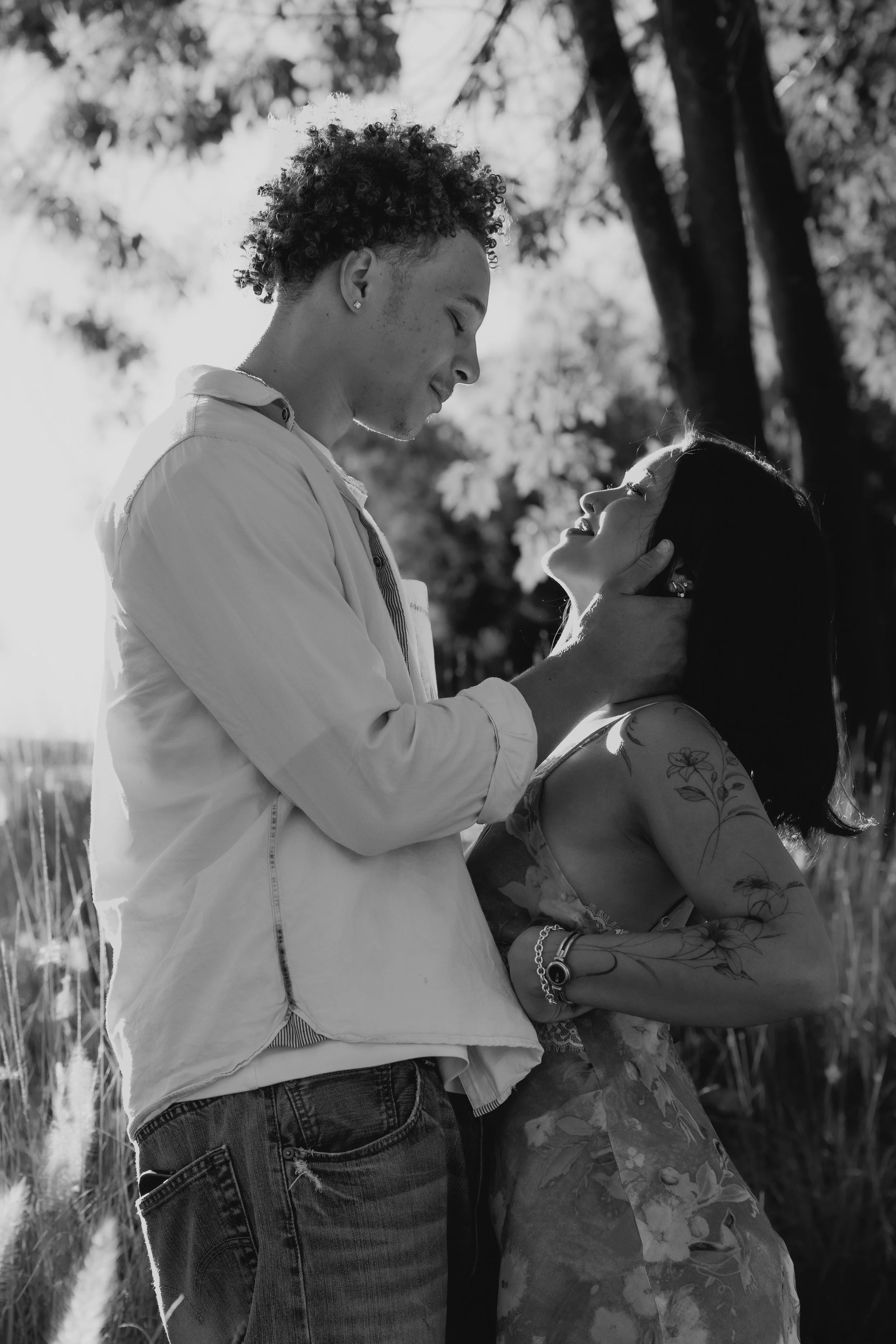 A man and woman standing outdoors under a tree, looking at each other with affectionate expressions, black and white photograph