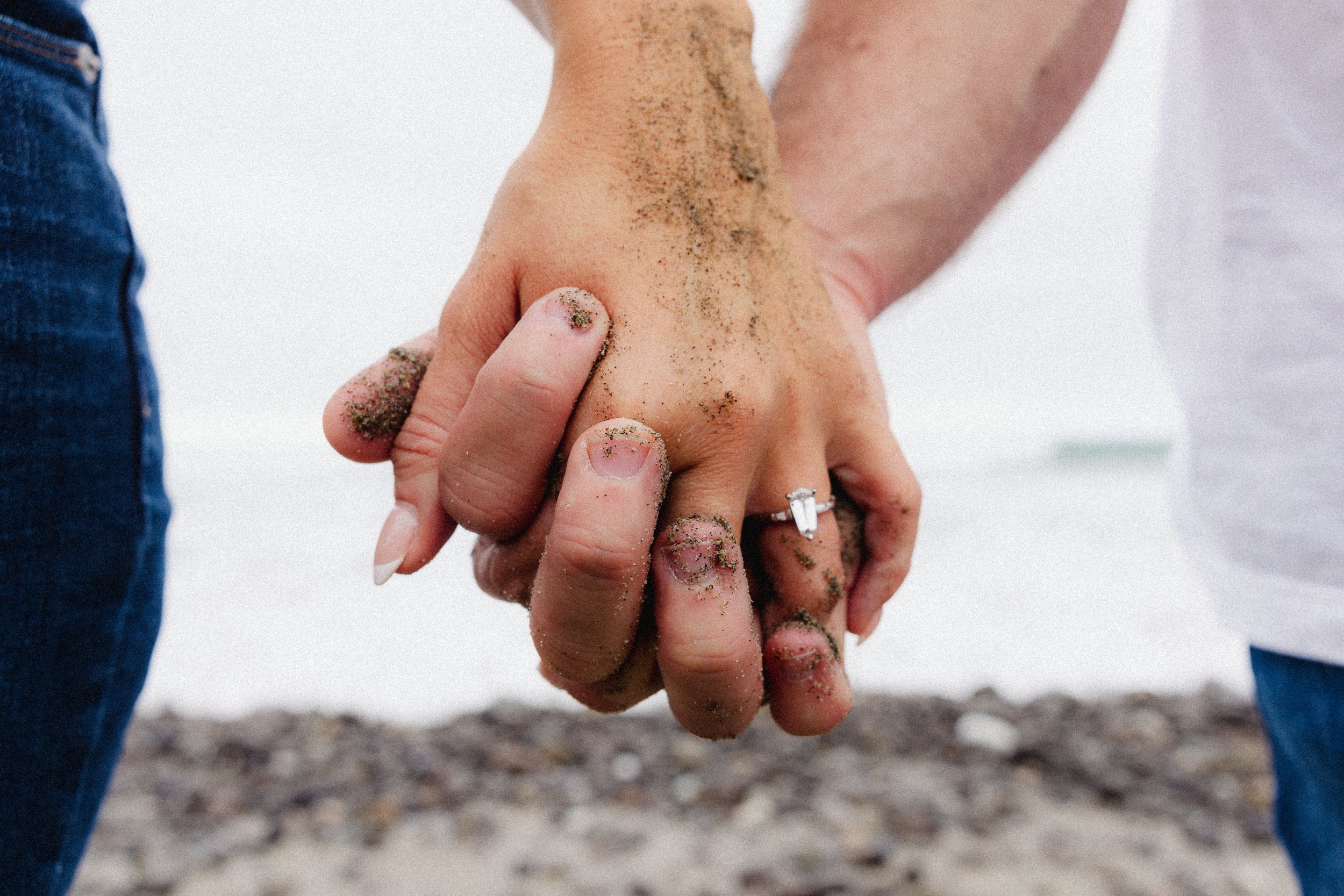 Two people holding hands covered in wet sand, standing on a beach.