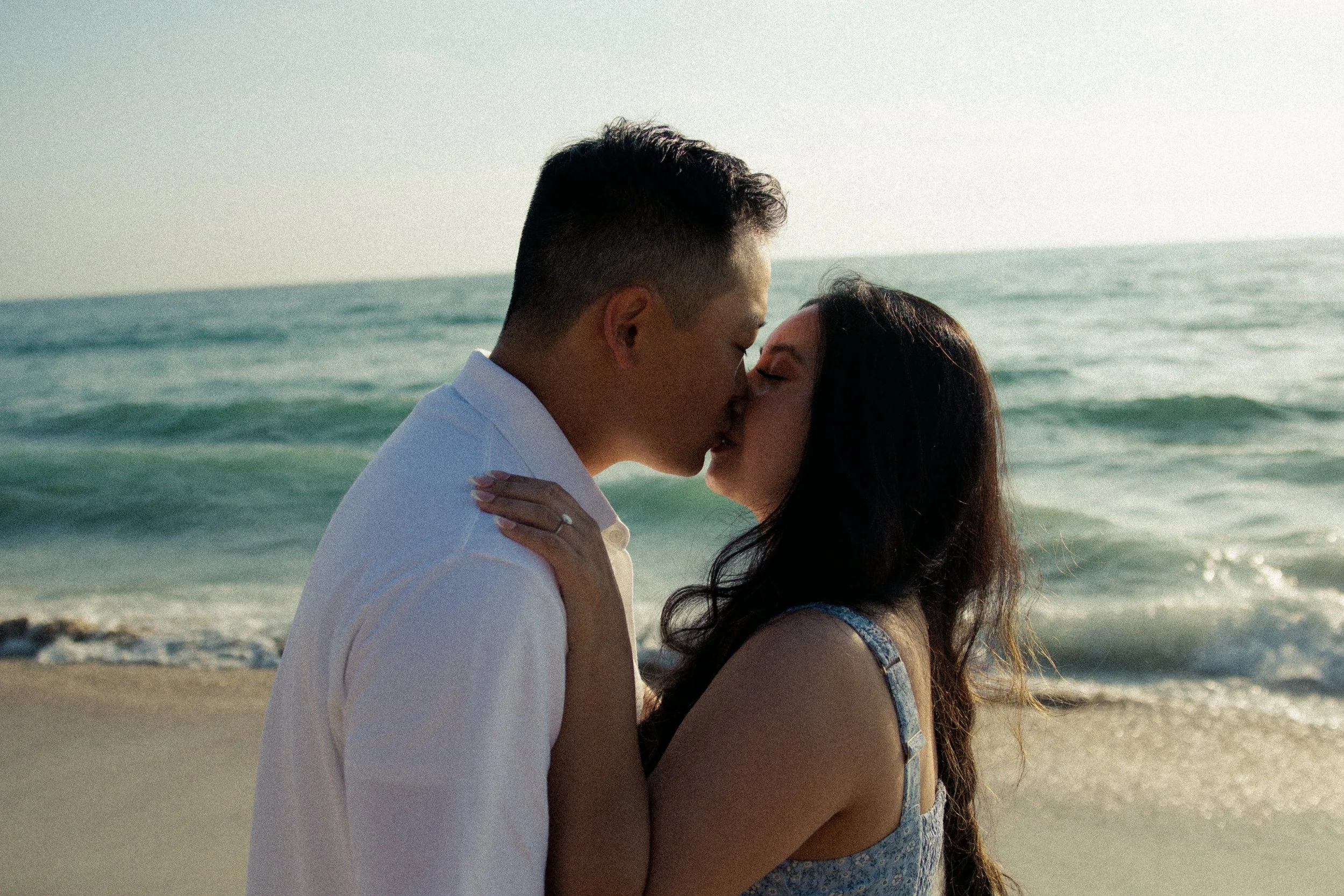 A couple kissing on the beach near the ocean during sunset.