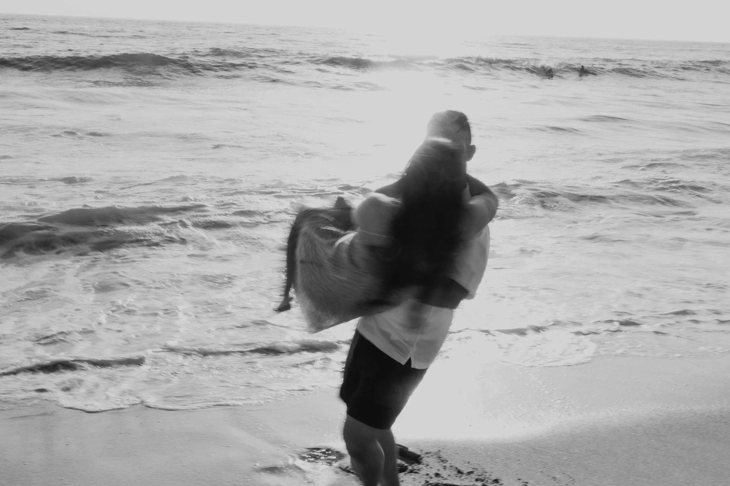A person standing on the beach, holding a large fish in their arms, with the ocean and waves in the background.