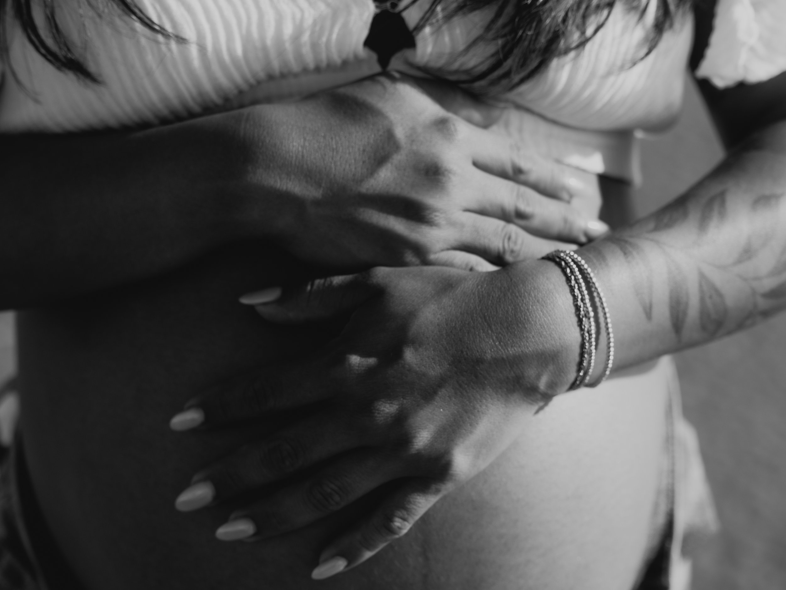 Close-up of two people's hands resting on a surface, one with a bracelet, in black and white. One hand gently placed on top of the other.