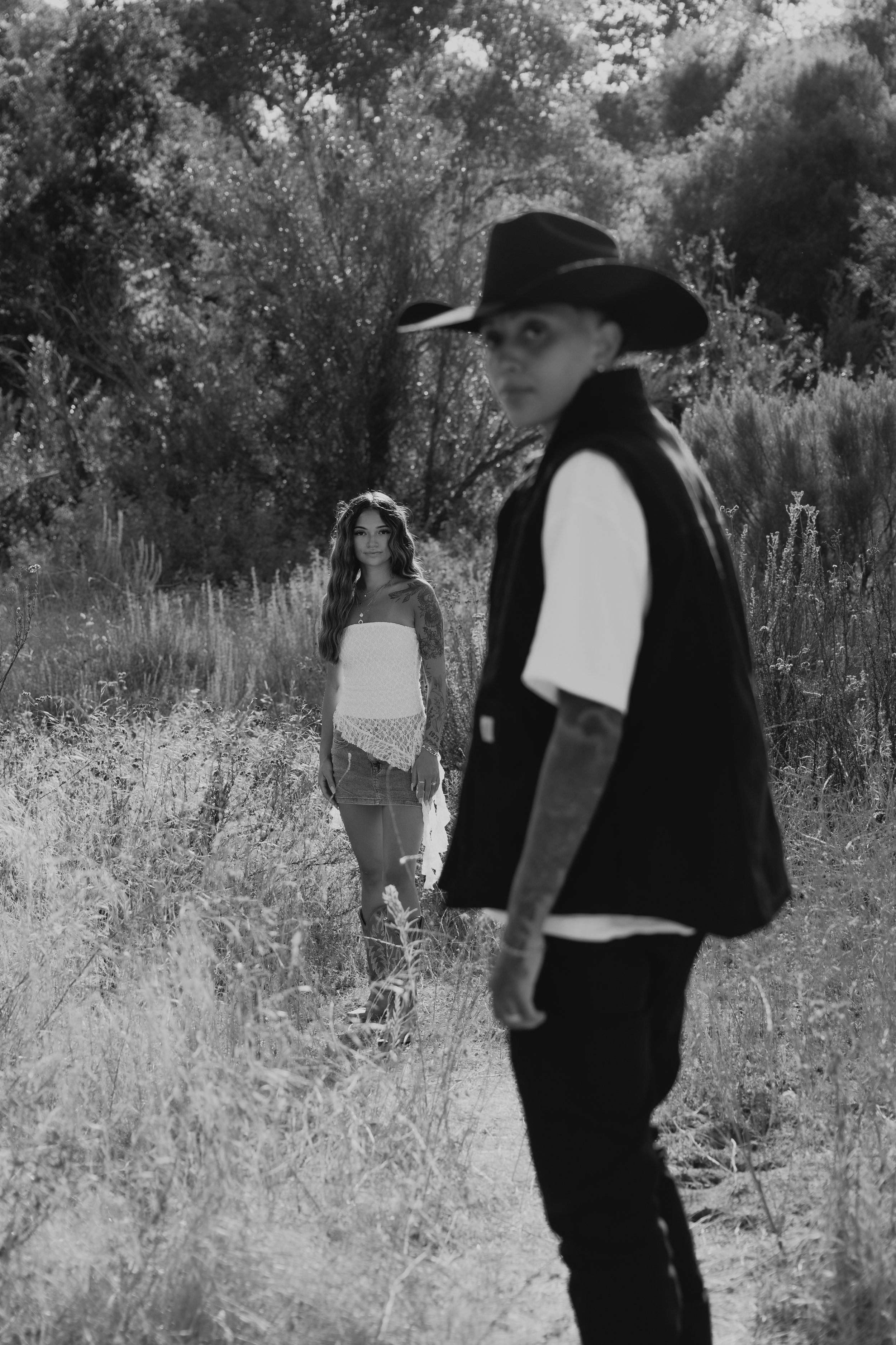 A woman and a man outdoors in a natural setting with tall grass and trees, black and white photo.