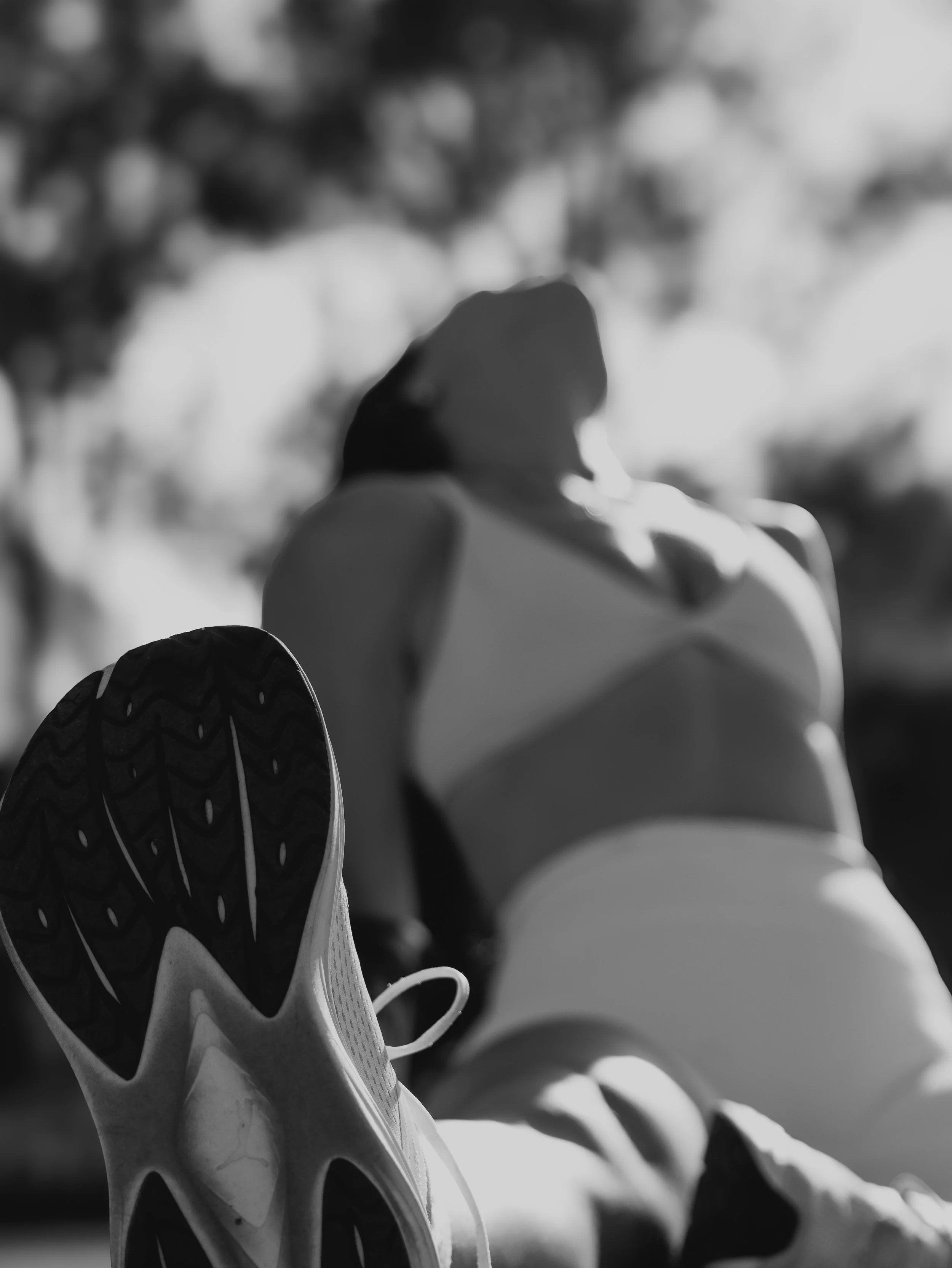 Close-up of a white sneaker with black soles, viewed from the side, with a blurred outdoor background.