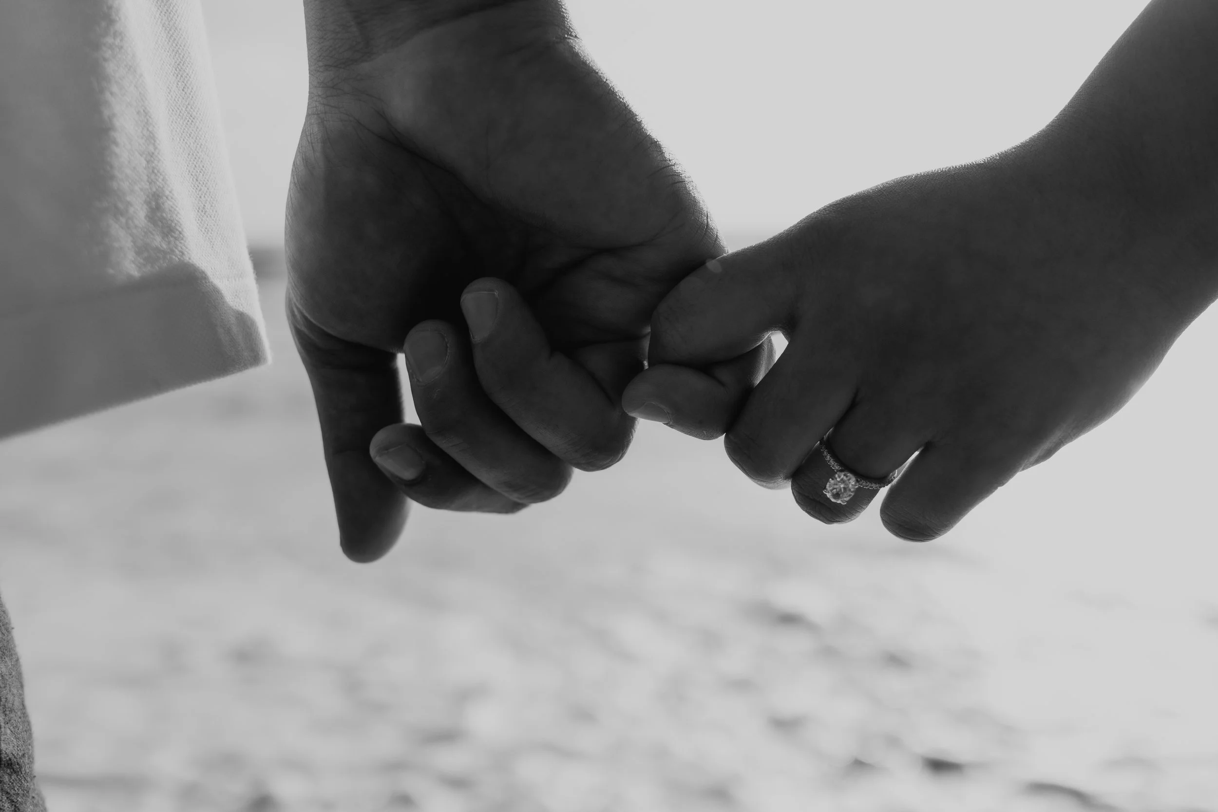 Two people holding hands, with one person's hand resting gently on top of the other's hand, close-up in black and white.