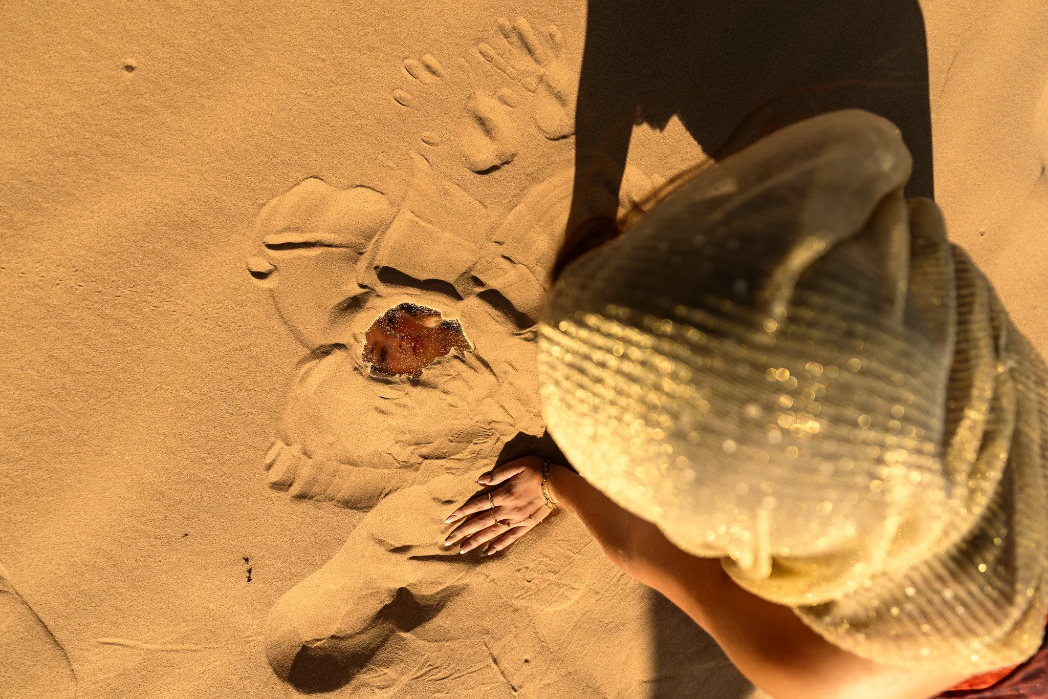 A sand drawing of a crab with a person’s hand and leg visible in the foreground at the beach.