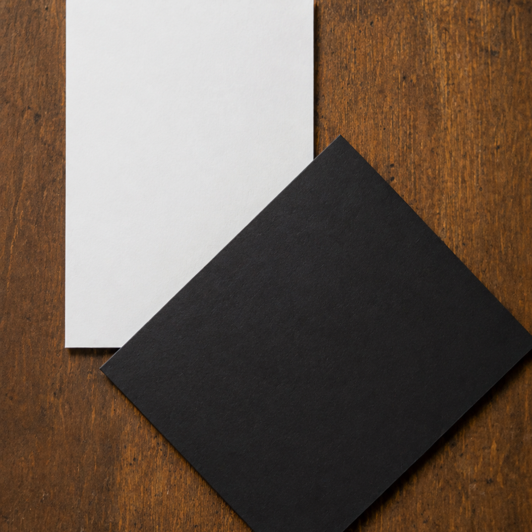 Two cards, one white and one black, placed on a wooden surface, with the black card tilted.