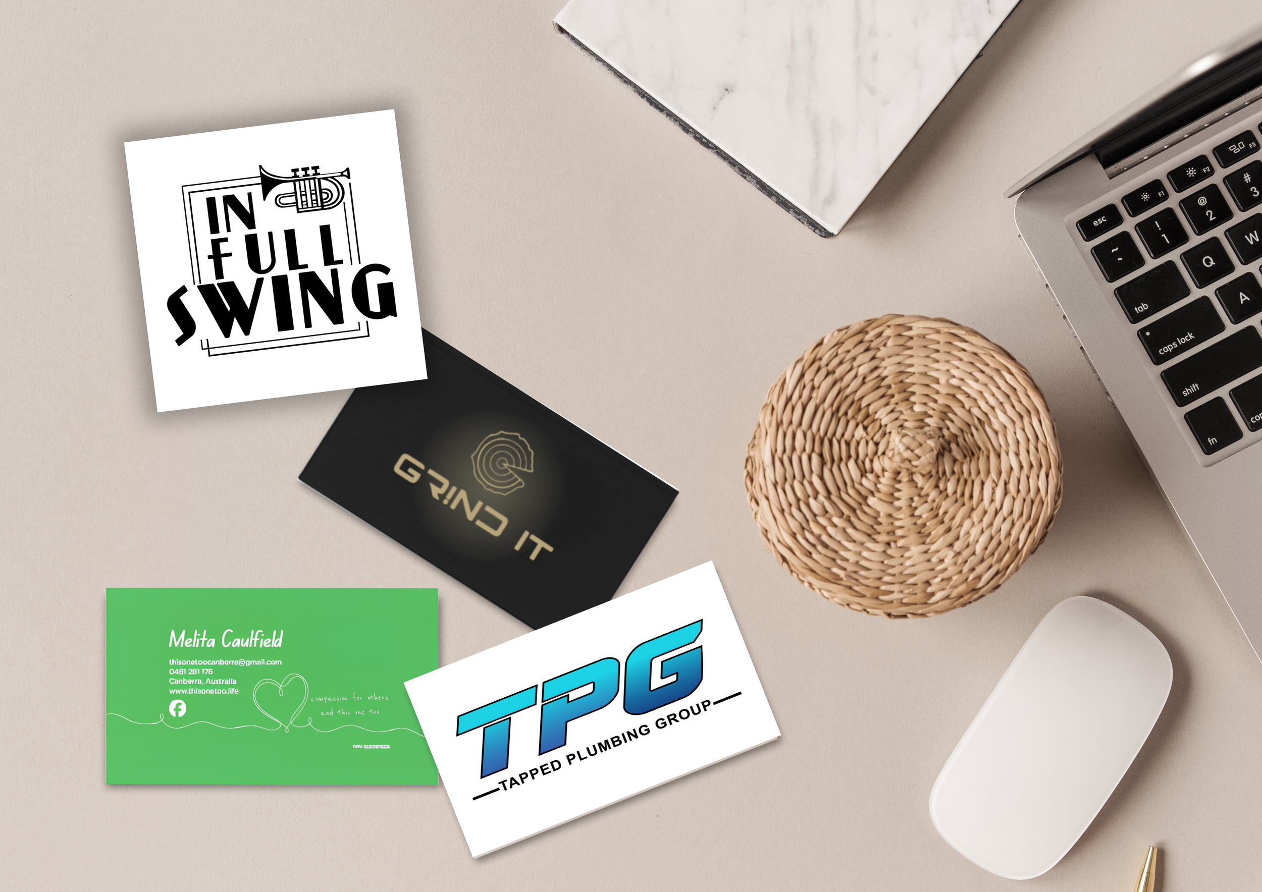 A beige desk with various business cards, a laptop, a woven coaster, and a white mouse.