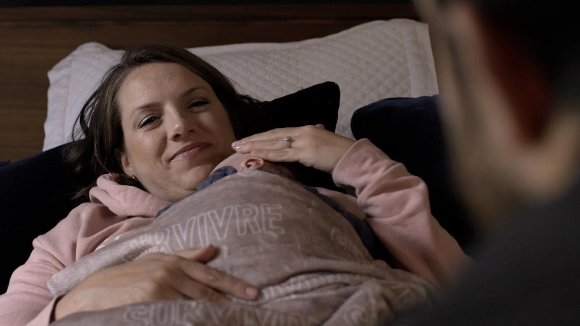 Image of Lorelei Colber hugging her newborn baby laying in bed. On the blanket wrapping her baby it reads SURVIVRE.