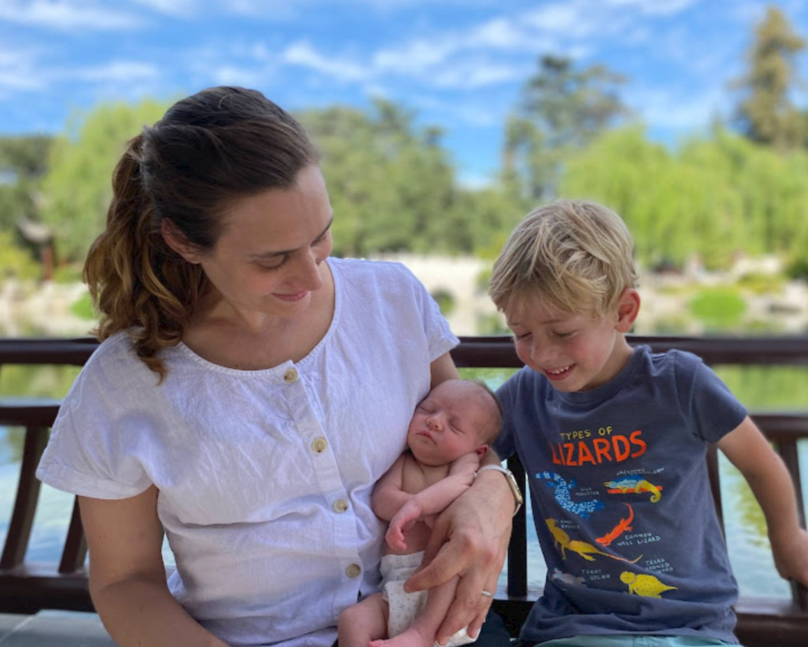 A woman holds her newborn child next to her son who is a few years older.