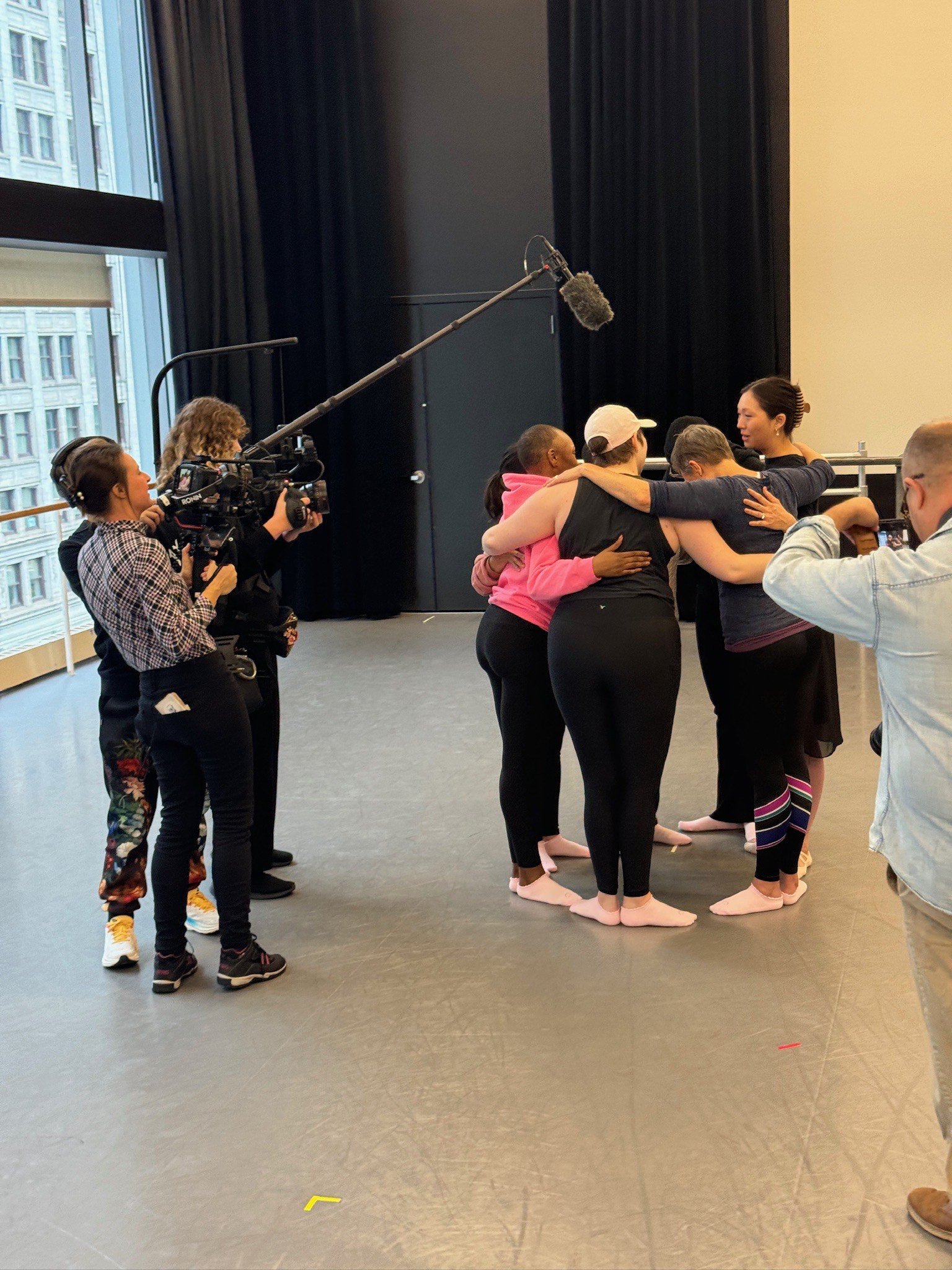 Group of people practicing social distancing and hugging indoors with a camera crew filming them.