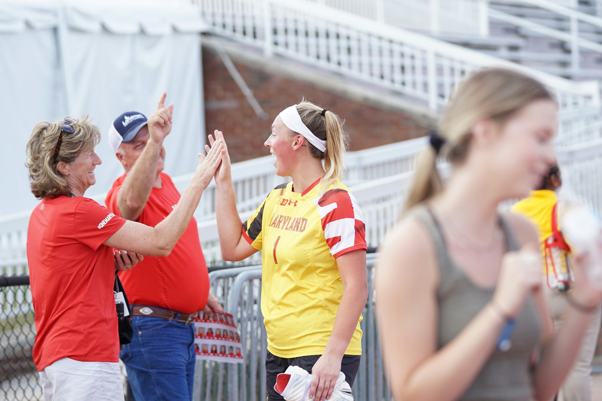 An athlete in a yellow sports uniform gives a high-five to smiling parents. Other athletes and spectators are blurred in the foreground and background.