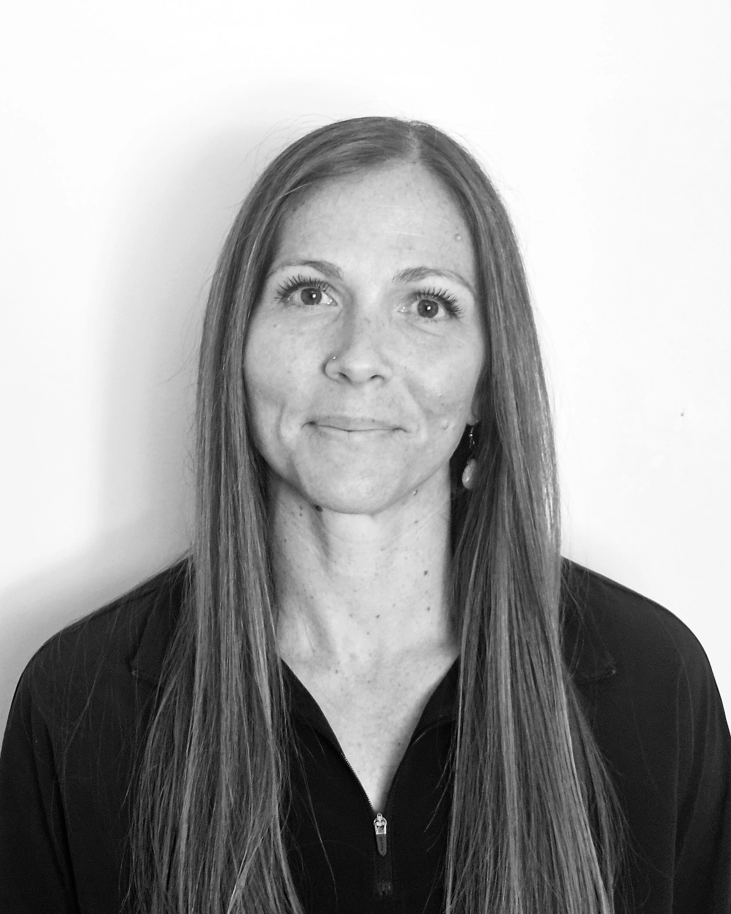 CEO and owner, Sonja, with long straight hair, wearing a zip-up jacket, looking upwards with a slight smile, against a plain white background.