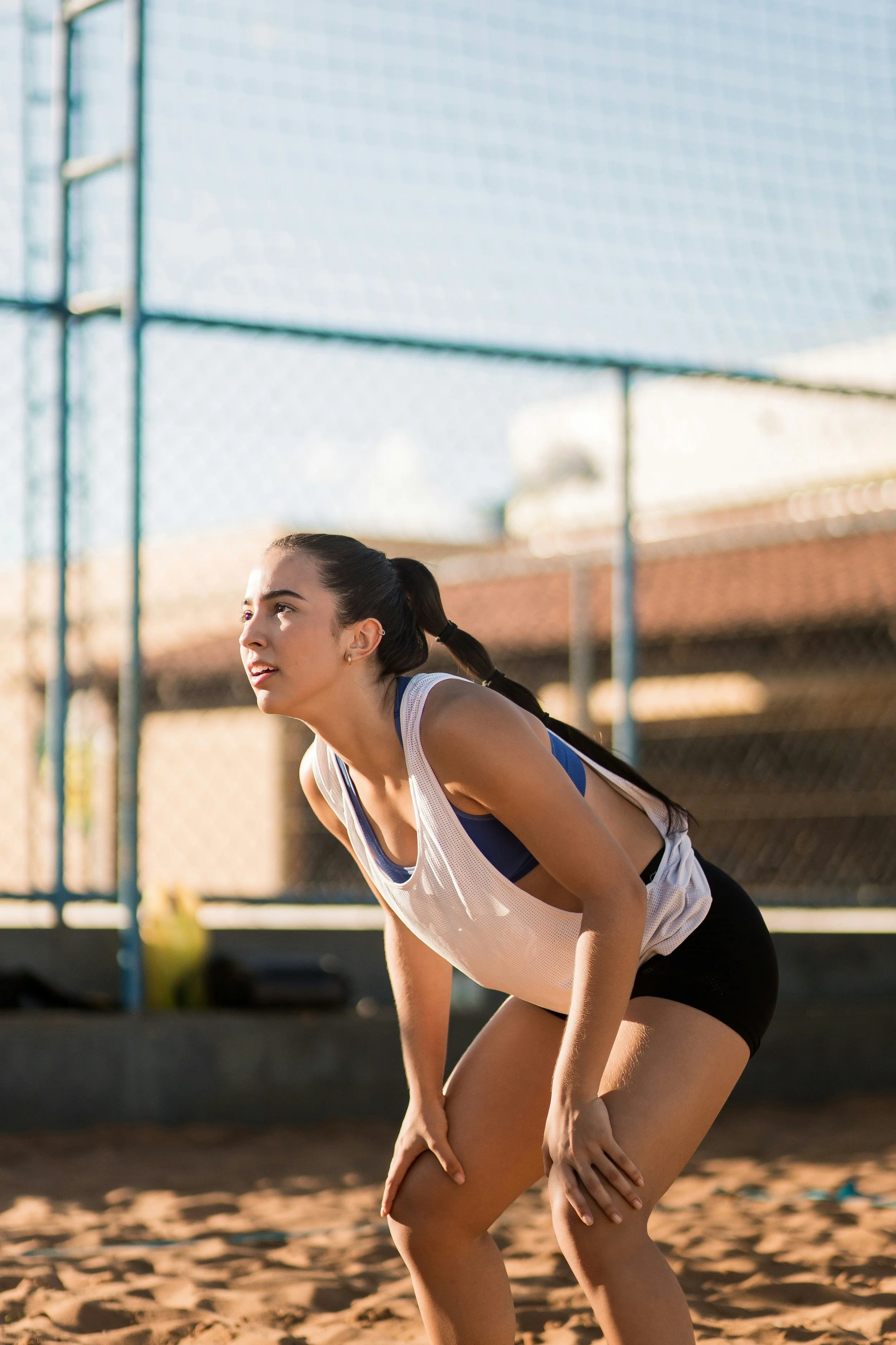 Young female volleyball player in a ready position on an outdoor sandy volleyball court.