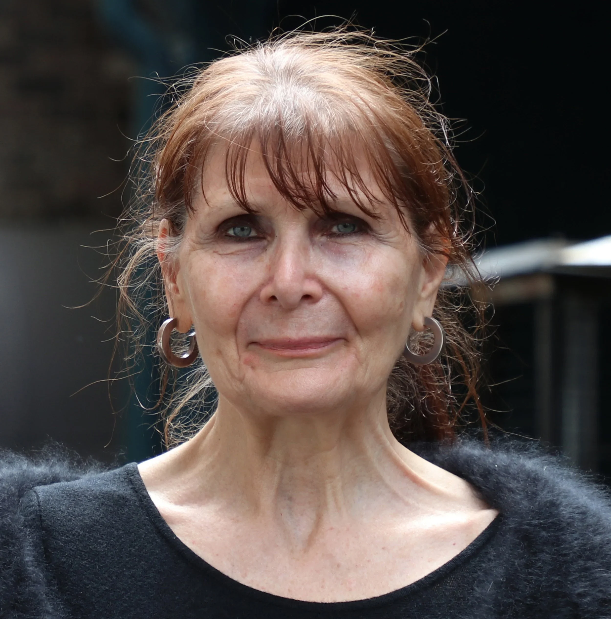 Close-up of a woman's face showing her eyes, hair, and part of her black shirt with silver hoop earrings.