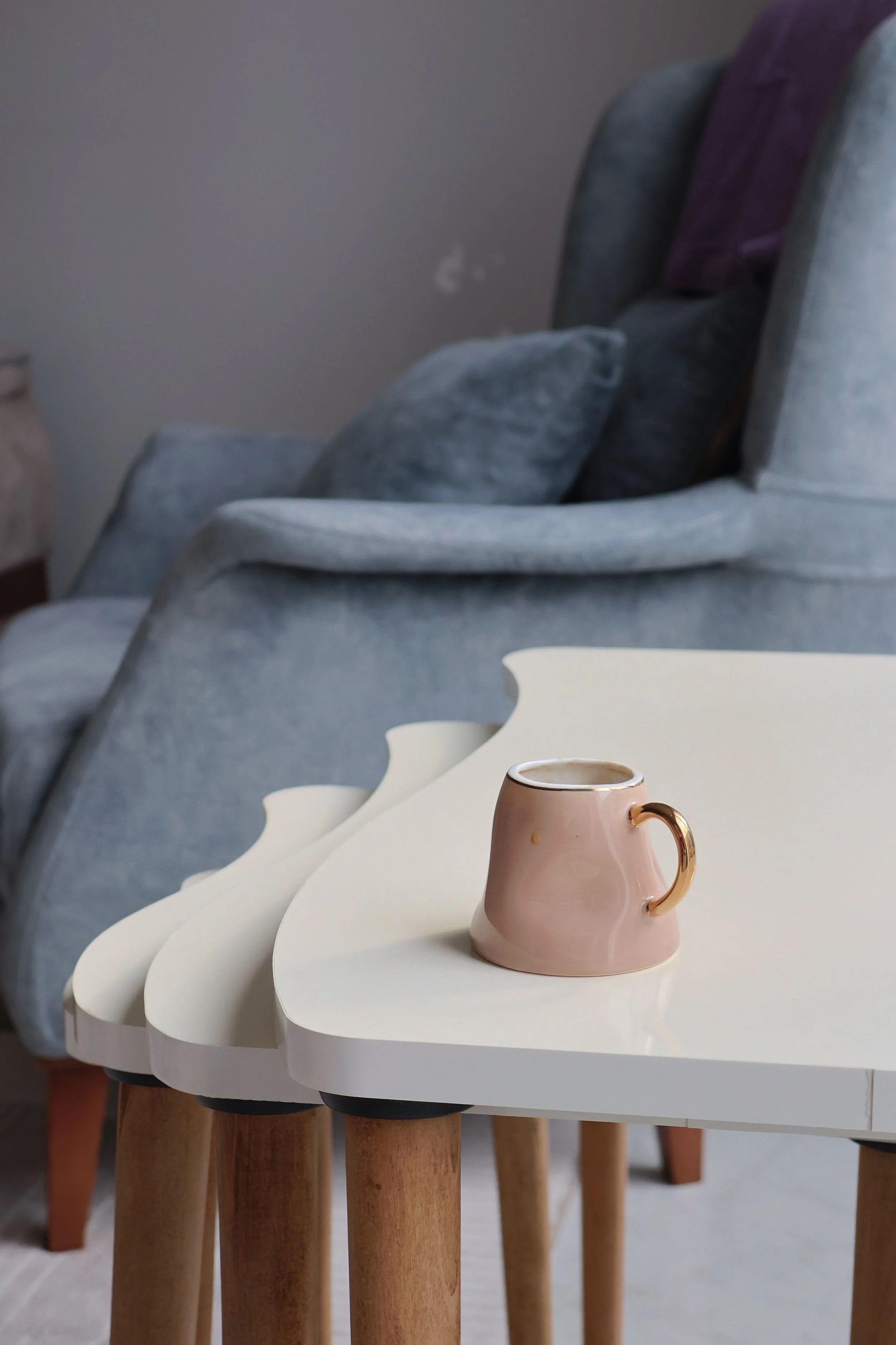A beige ceramic mug with a gold handle sitting on a white wavy-edged table.