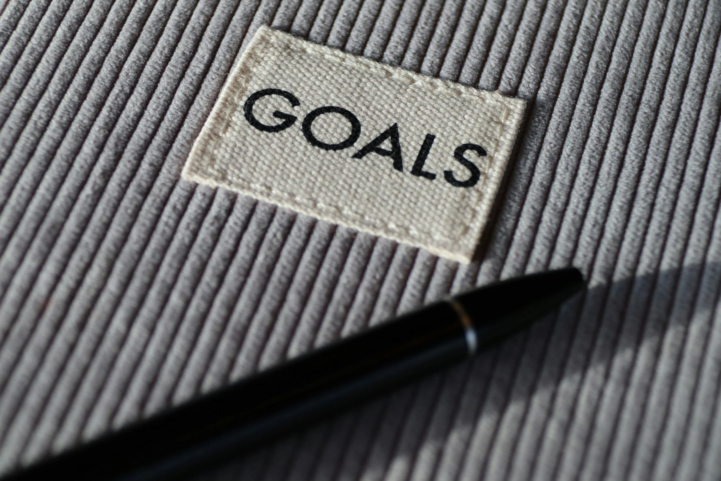 A clothing label on a gray, ribbed fabric with the word 'GOALS' embroidered in black.