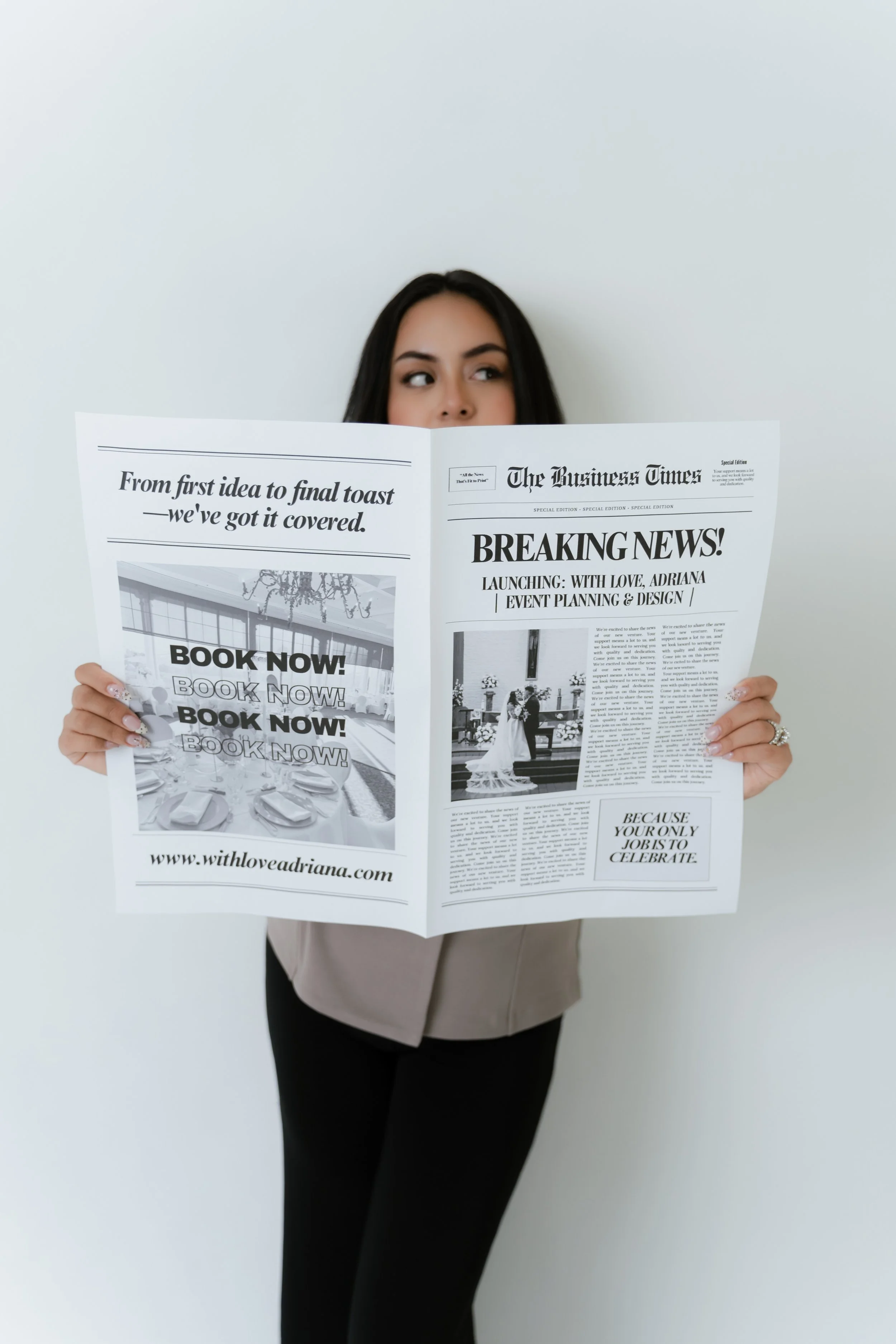A woman with dark hair holding a newspaper with headlines about a launch event. She is standing against a plain, light-colored background.