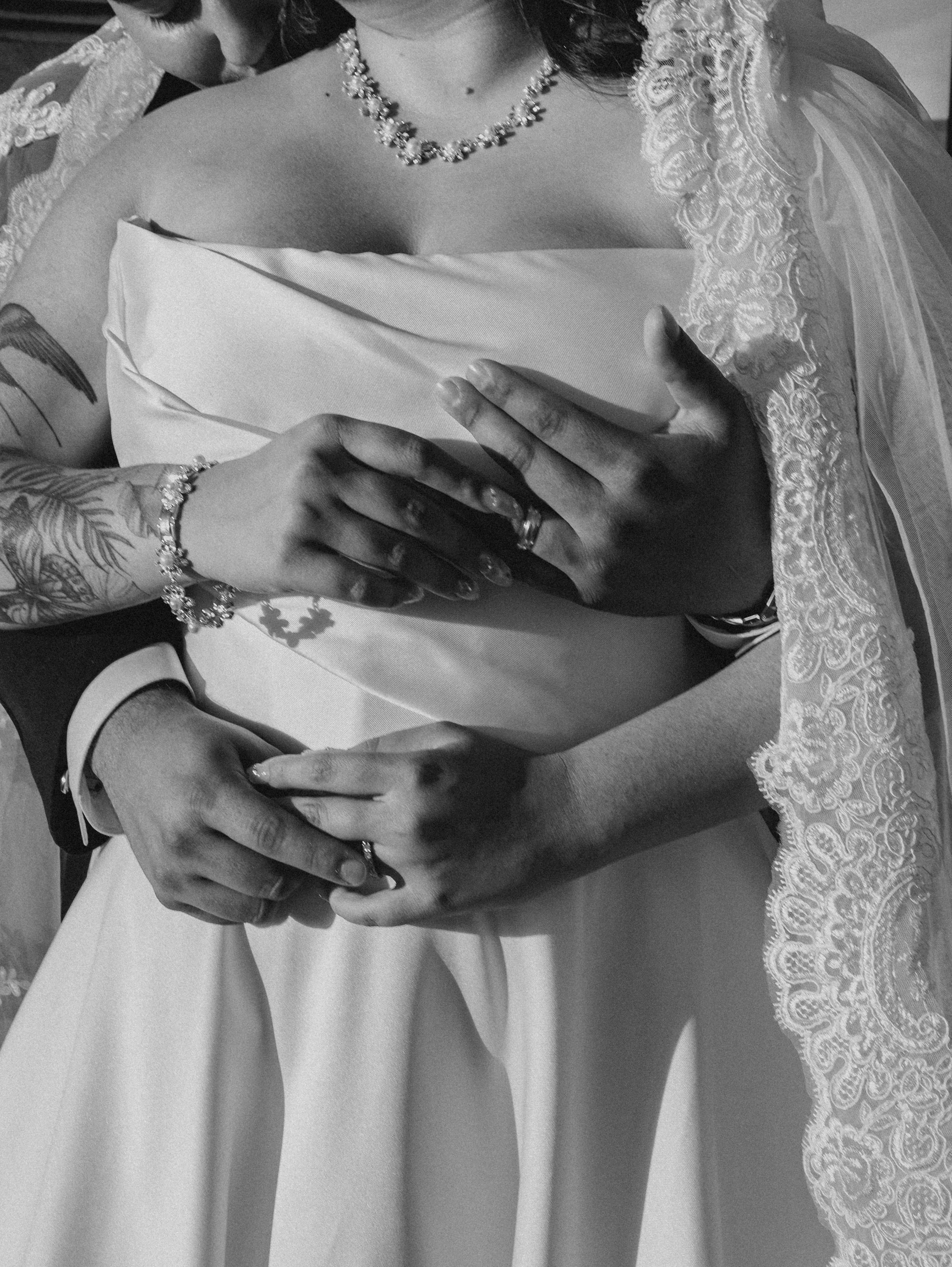 Woman wearing lace admiring herself in a mirror, with jewelry and tattoos visible on her hands and arms.