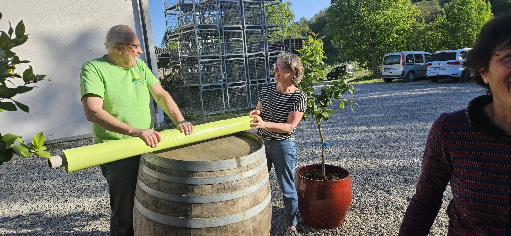 Zwei Frauen und ein Mann beim Austausch eines großen, gelben Kunststoffrohres, im Hintergrund Garten und Parkplätze.