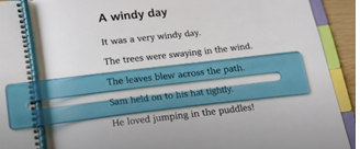 Open notebook with a story titled 'A windy day' and blue highlighted text reading 'The leaves blew across the path' and 'Sam held on to his hat tightly.'