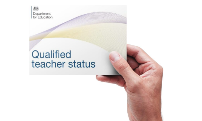 A hand holding a card that reads "Qualified teacher status" from the Department for Education.