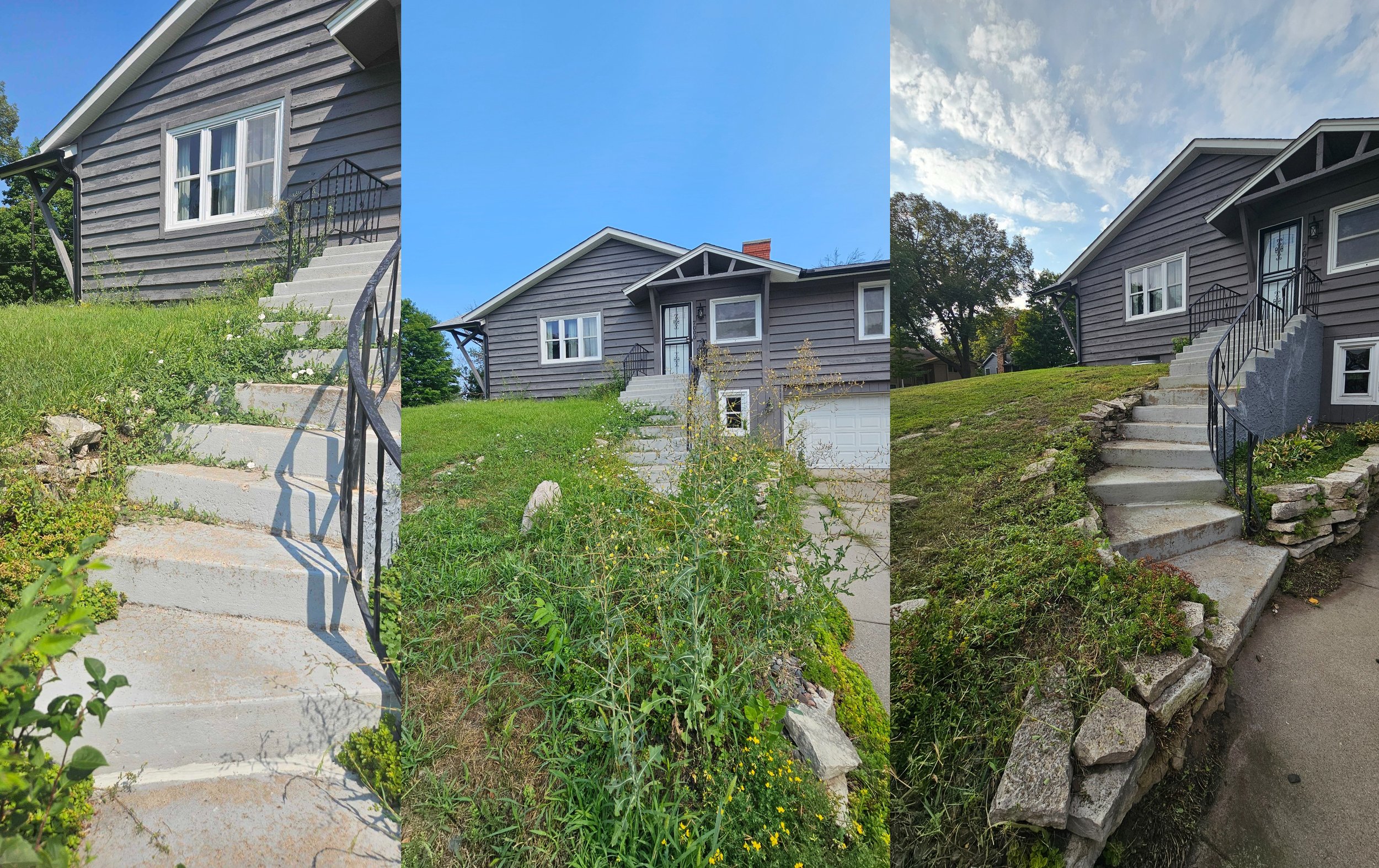 A house with gray wooden siding, white-framed windows, concrete stairs leading to the front door, a grassy yard with some plants and rocks, and a partly cloudy sky.
