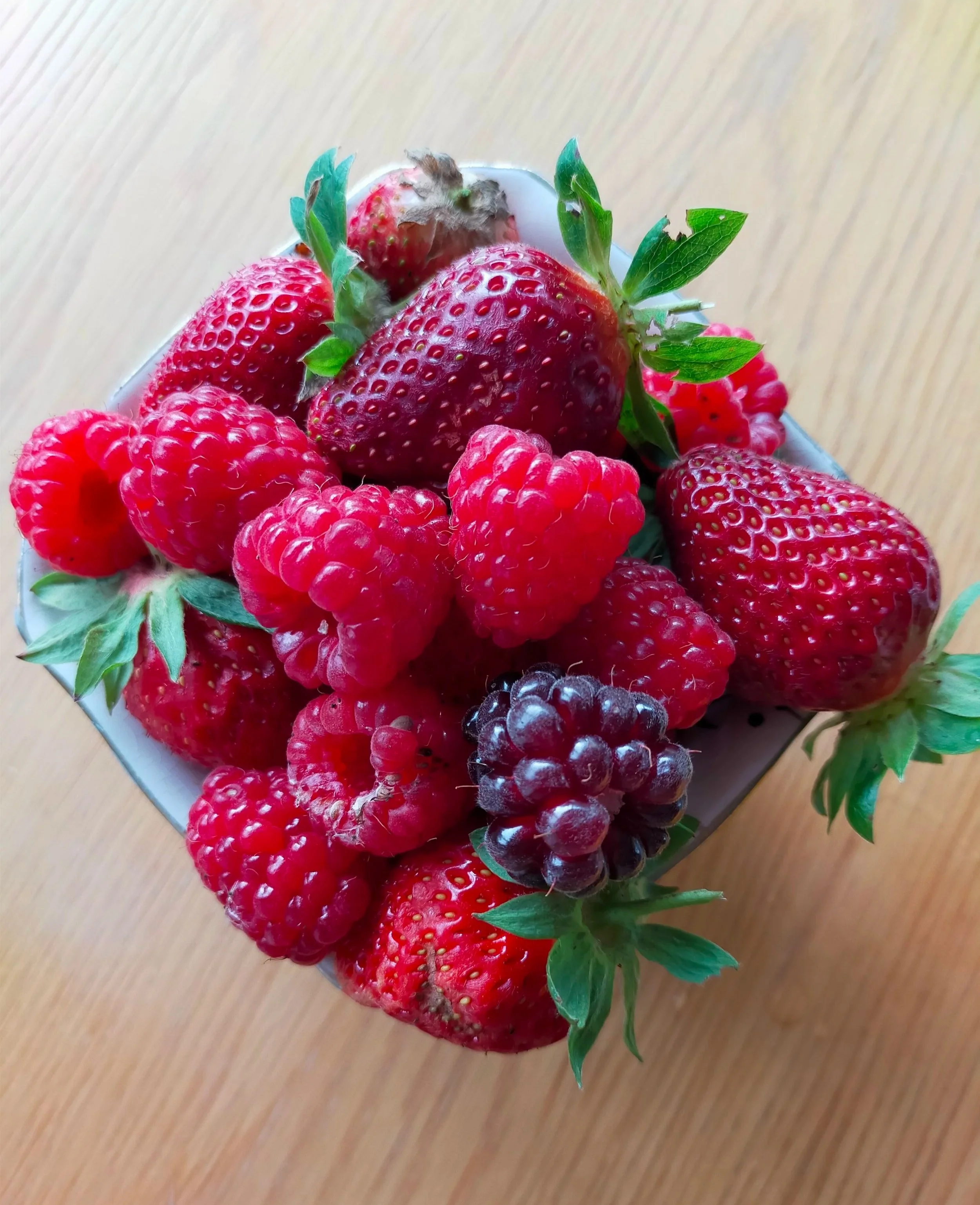 Close-up of fresh strawberries, raspberries, and blackberries in a bowl on a wooden surface.