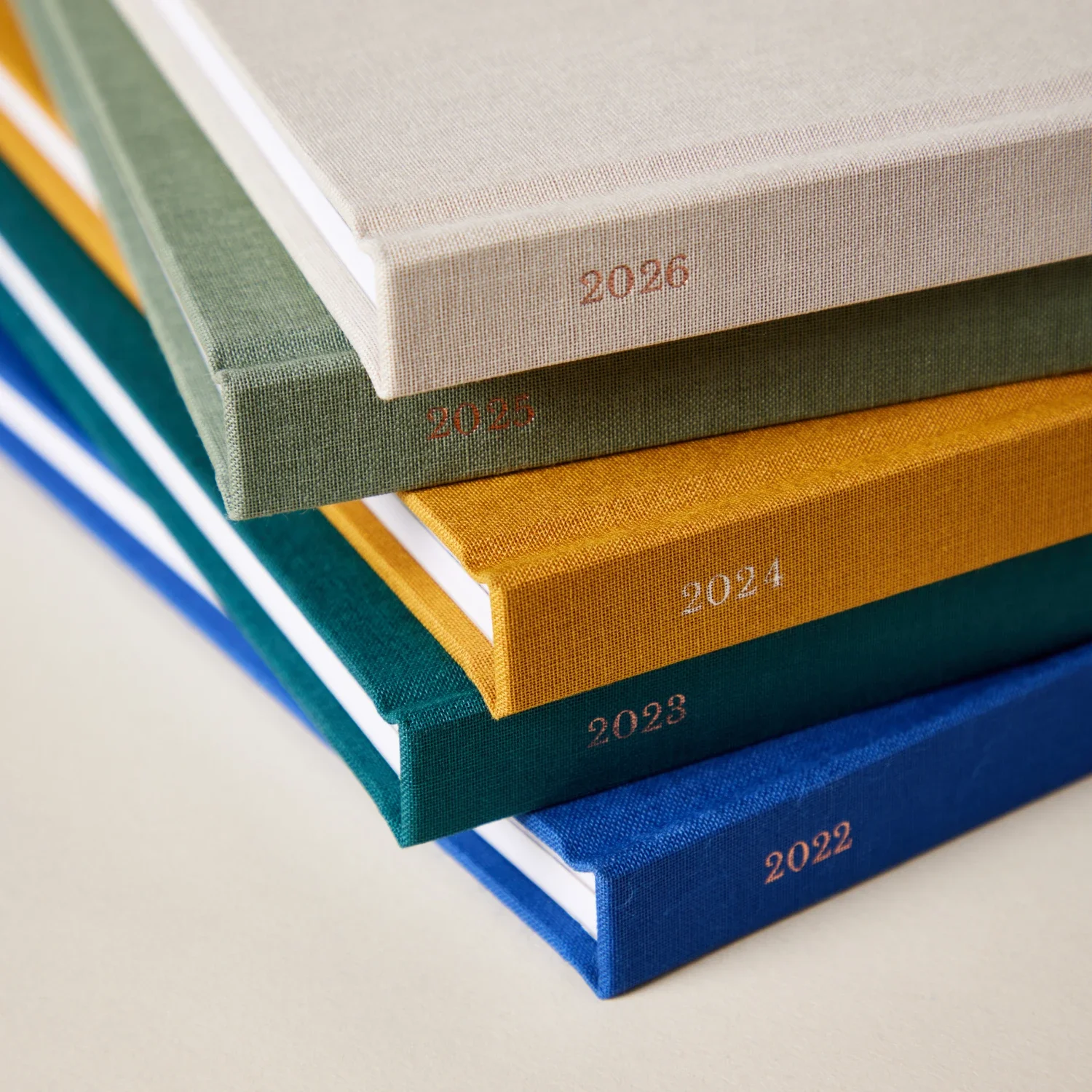 Une pile de cahiers colorés avec les années 2022 à 2026 imprimées en or sur leurs couvertures en tissu.