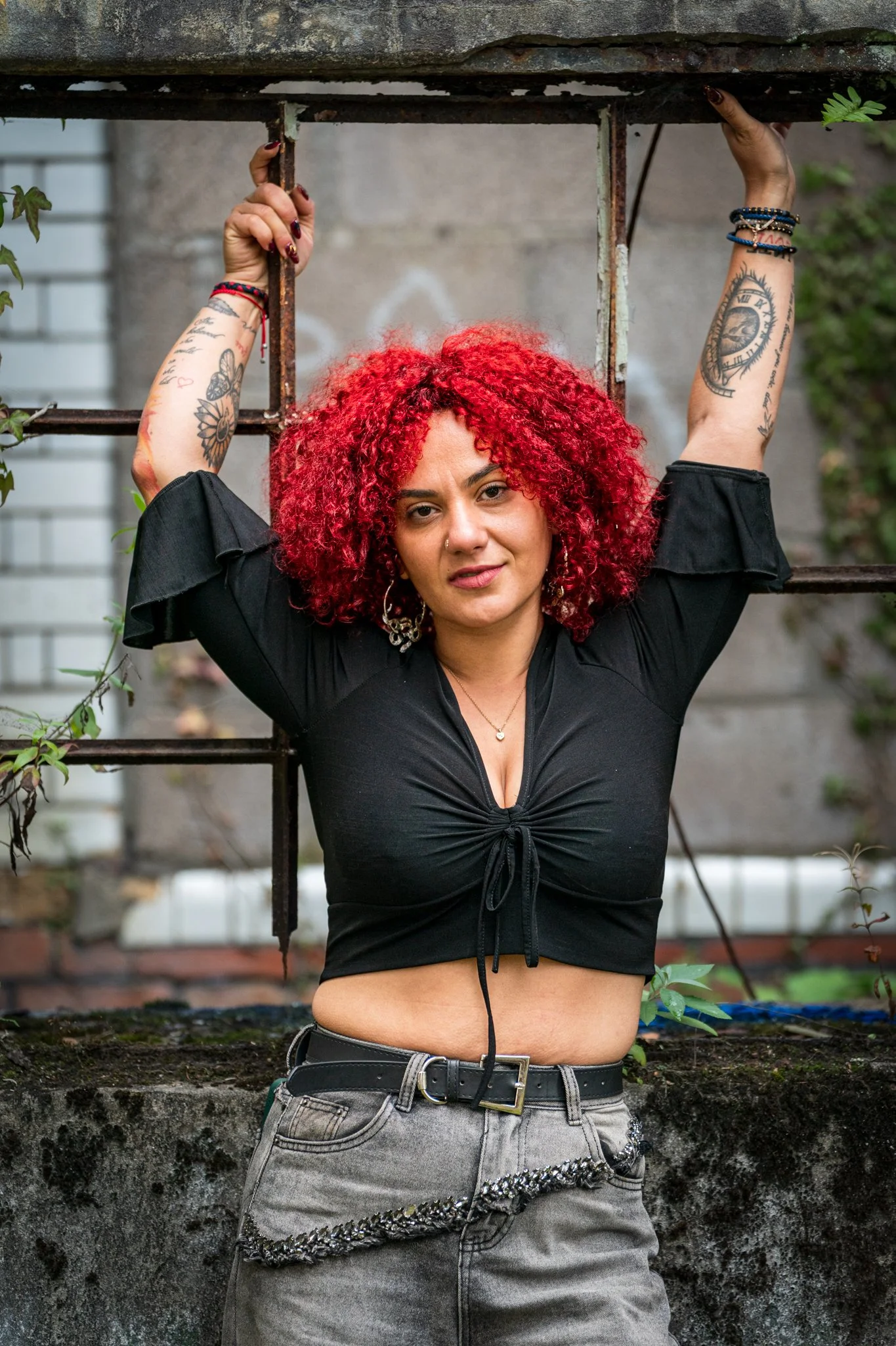 Tattooed woman with bright red curly hair posing against a rusted window frame at a derelict building — UskLight portrait photography, Newport