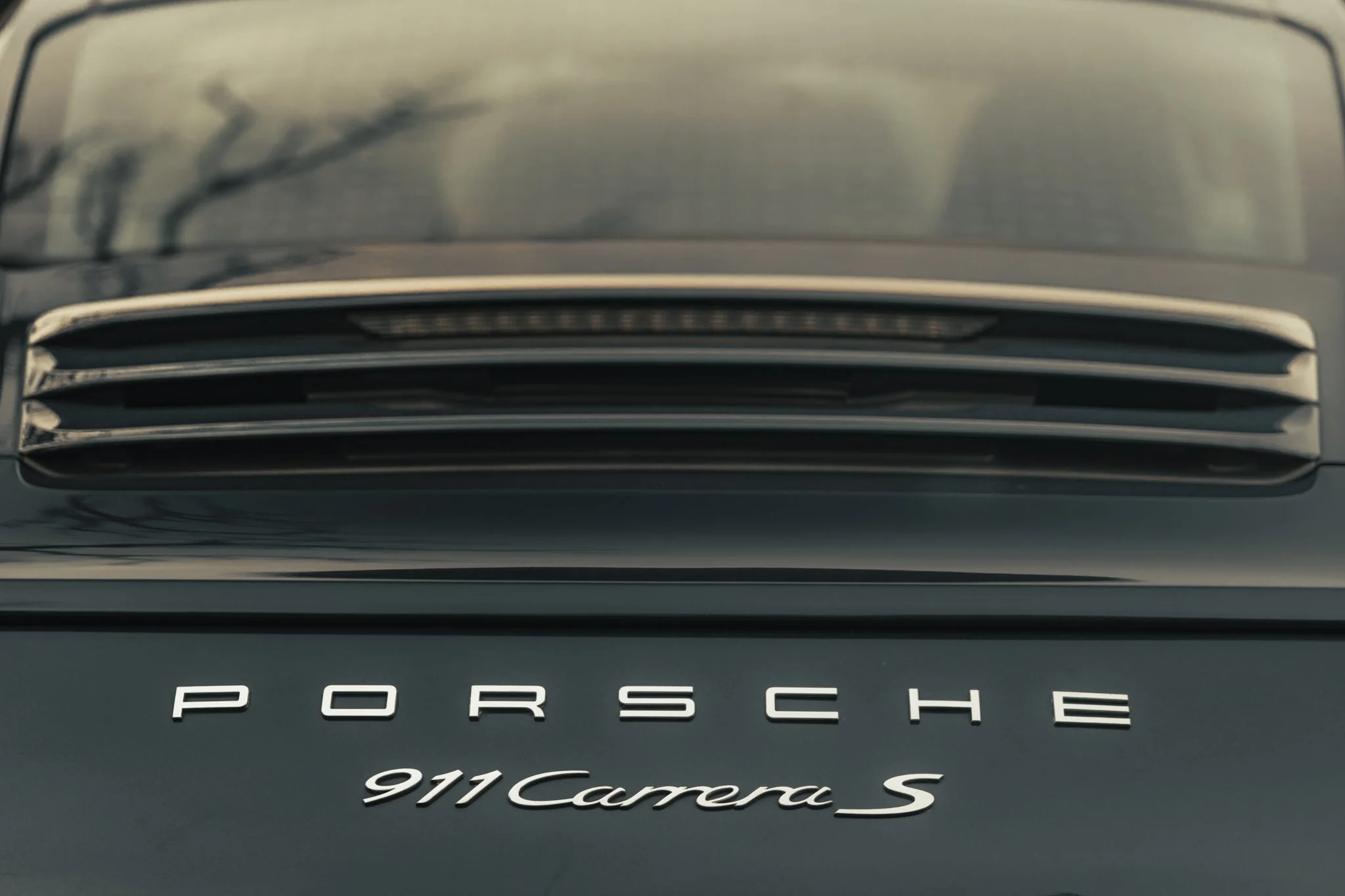 Close-up of the front grille of a black Porsche 911 Carrera S sports car, with the Porsche logo and model name visible.
