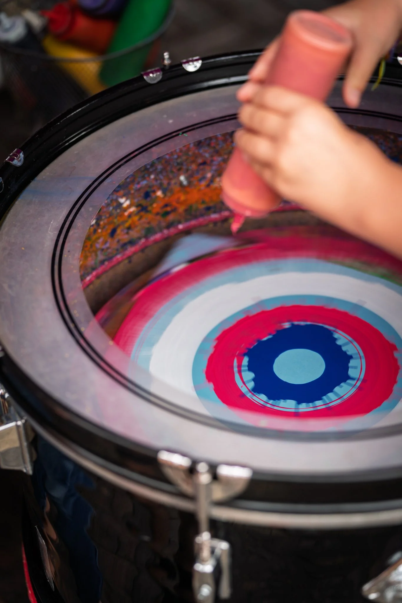 A person is using a squeegee to clean the interior of a colorful, circular art piece or design inside a circular frame. The design features concentric circles with vibrant colors including blue, white, red, and pink.