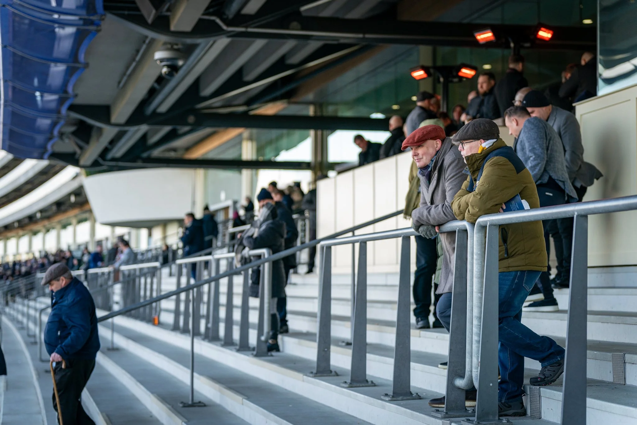 People waiting in line at an airport terminal, standing on the stairs and leaning on railings indoors.