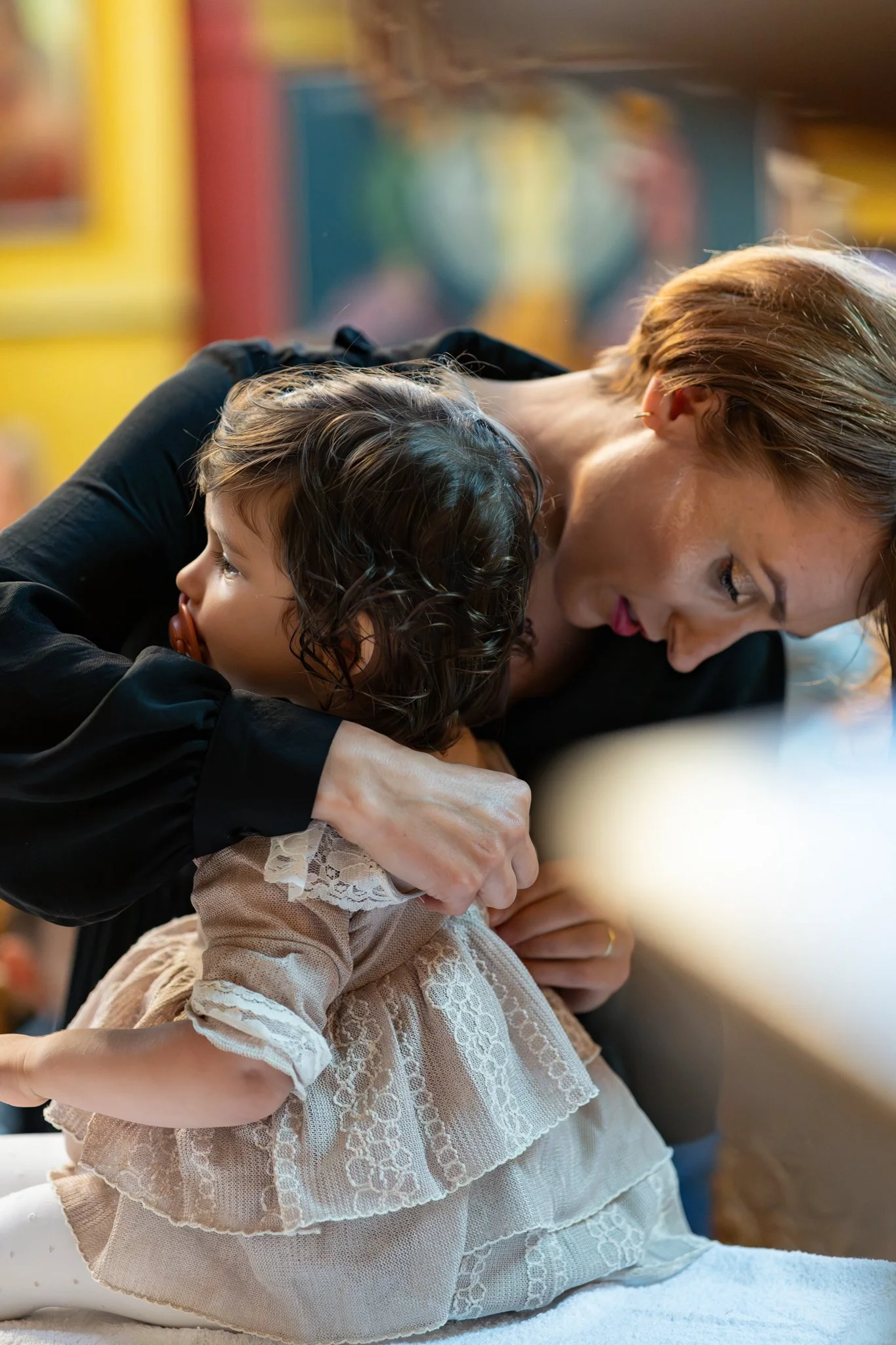 A woman and a young girl are embracing and praying together inside a colorful room.