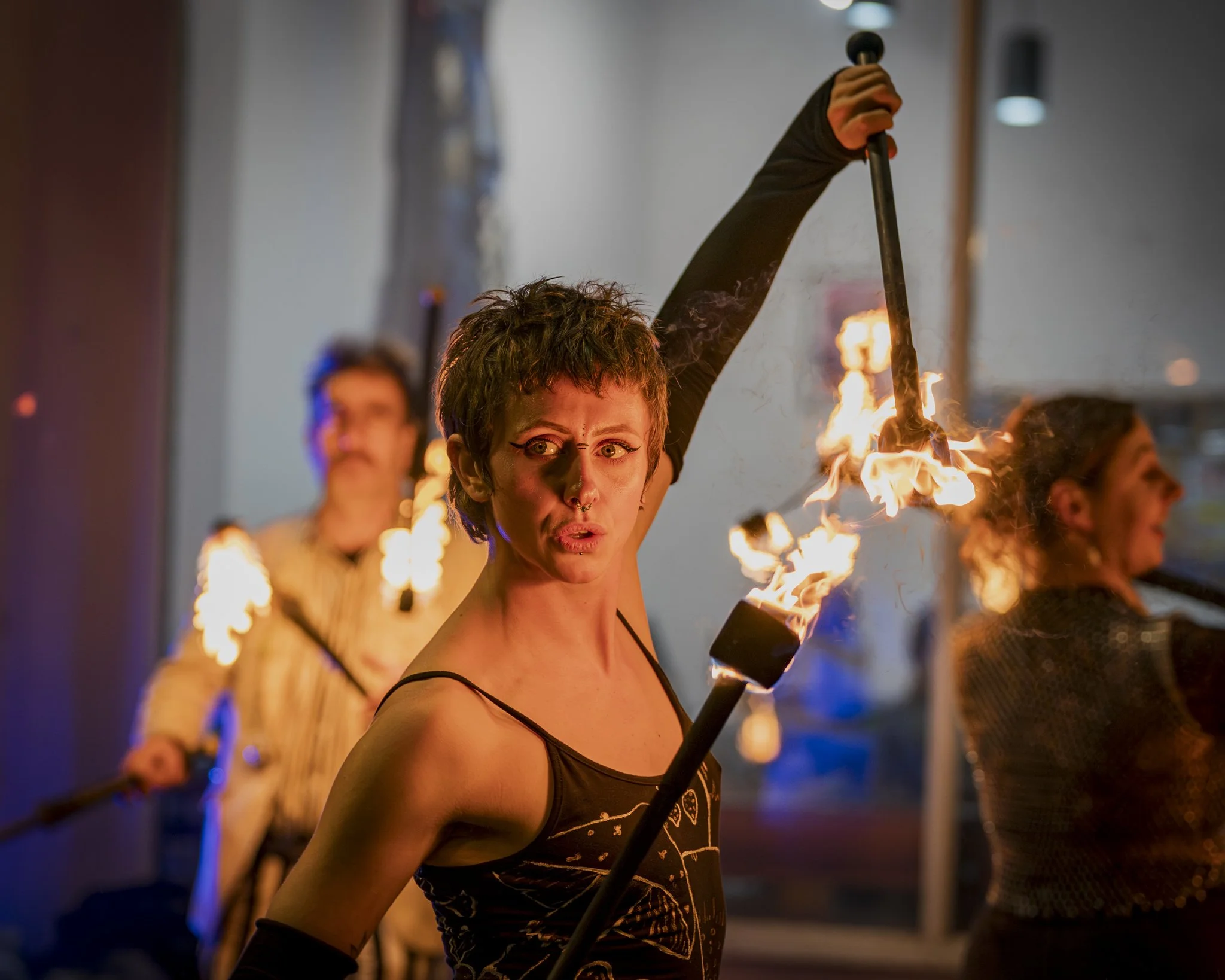 A woman with short hair and makeup holding a flaming torch at a glow performance event.