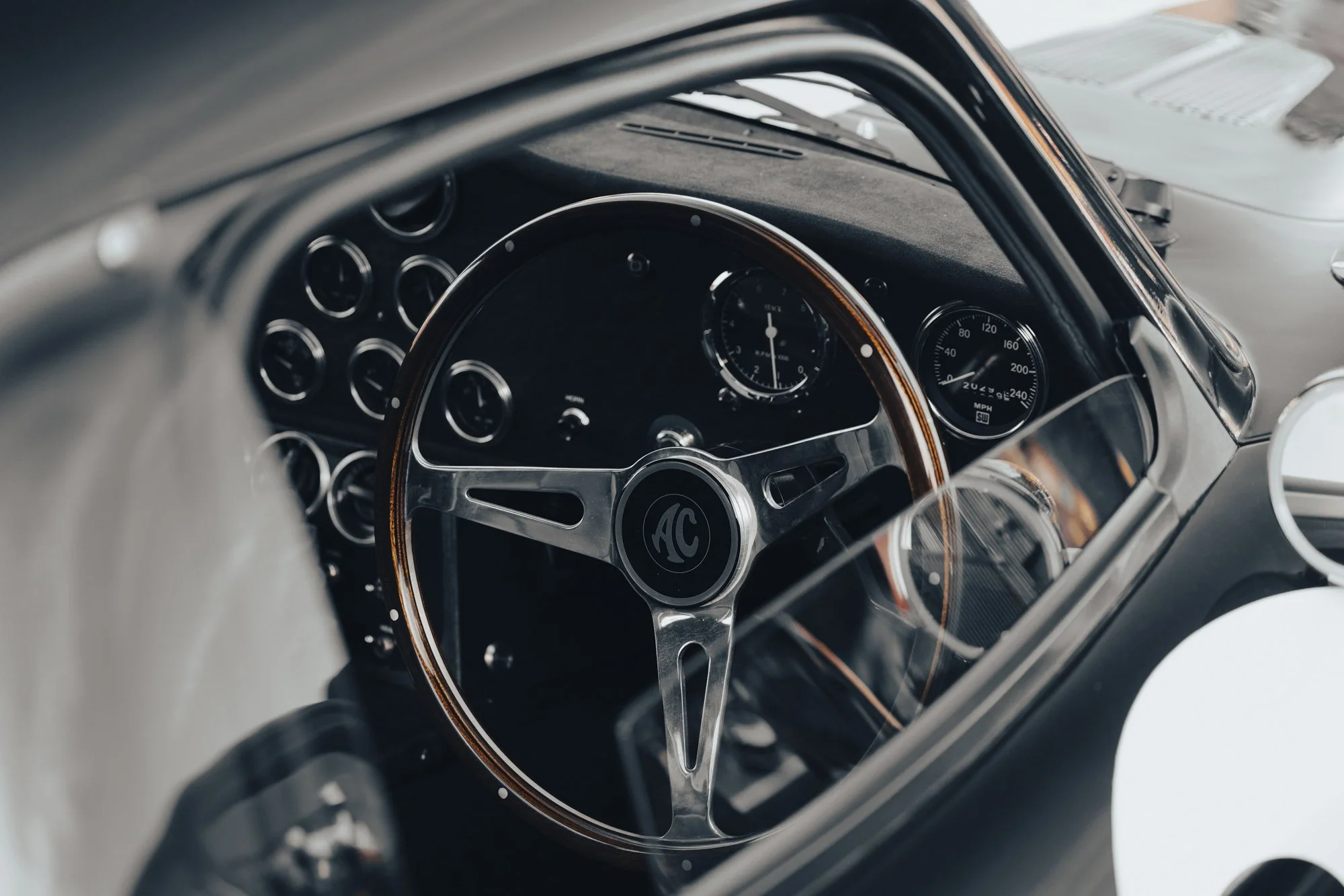 Close-up view of a vintage car's dashboard and steering wheel, featuring analog gauges and a wooden rim on the steering wheel.