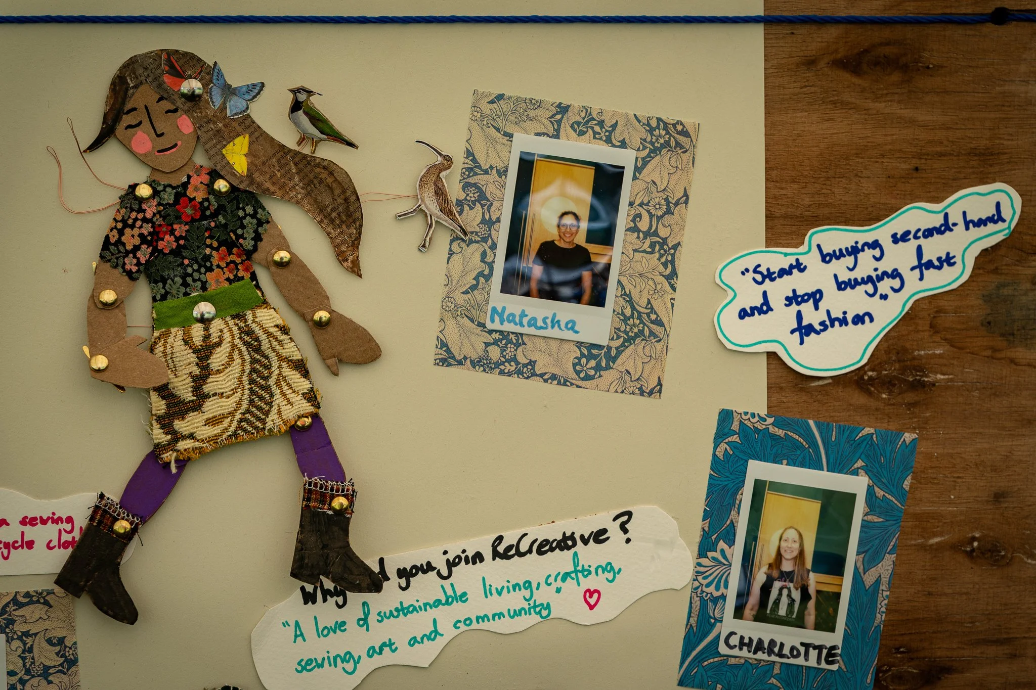 A wall display features a collage of artwork and photographs, including a cut-out paper doll of a girl with wings decorated with flowers and buttons, three ceramic or plastic bird figurines, a printed photo of a smiling woman labeled 'Natasha', and s