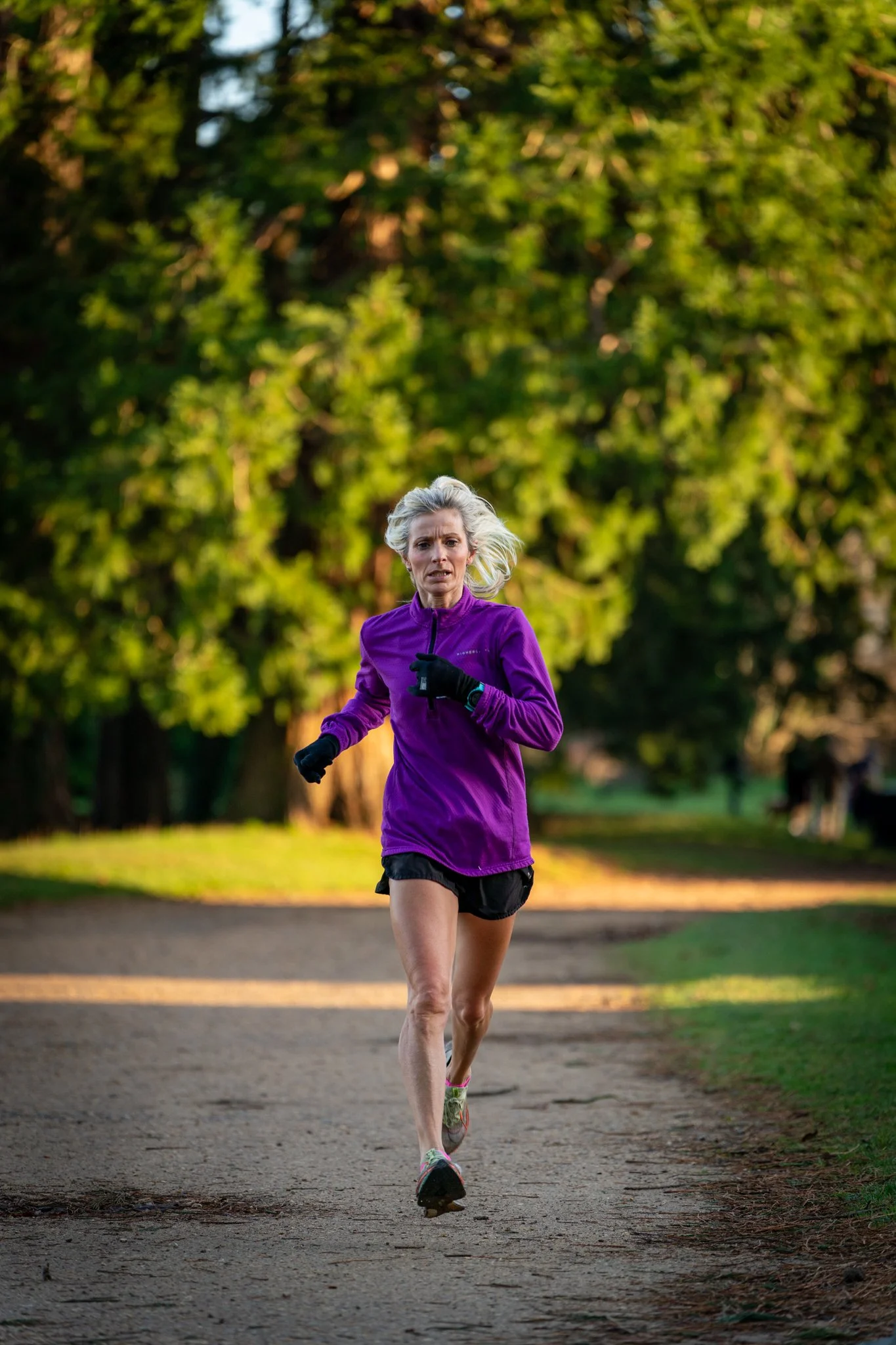 A woman in purple running clothes jogging on a park trail with trees in the background during daylight