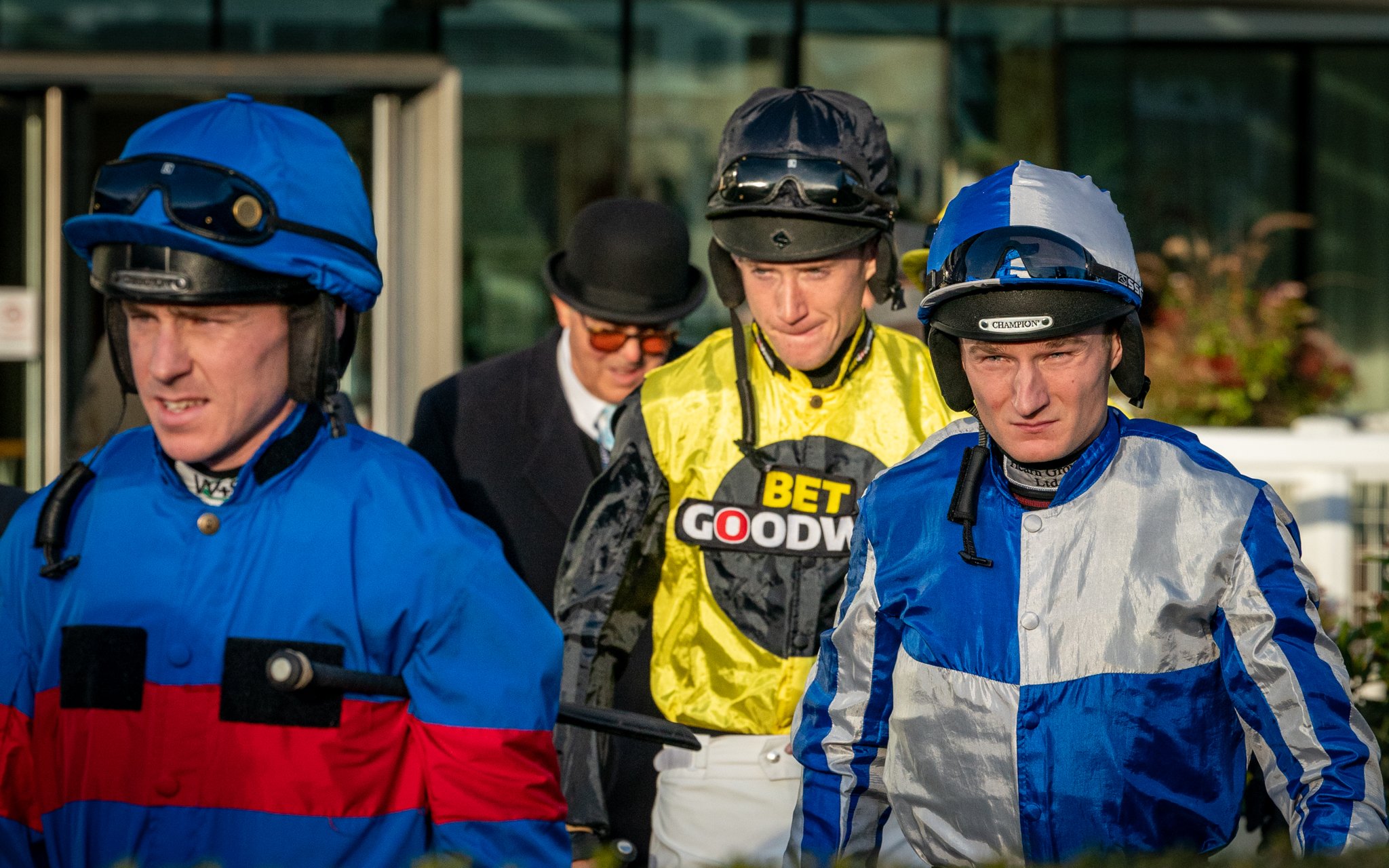 Jockeys and a trainer at a race track, wearing helmets and racing silks, preparing for a horse race.