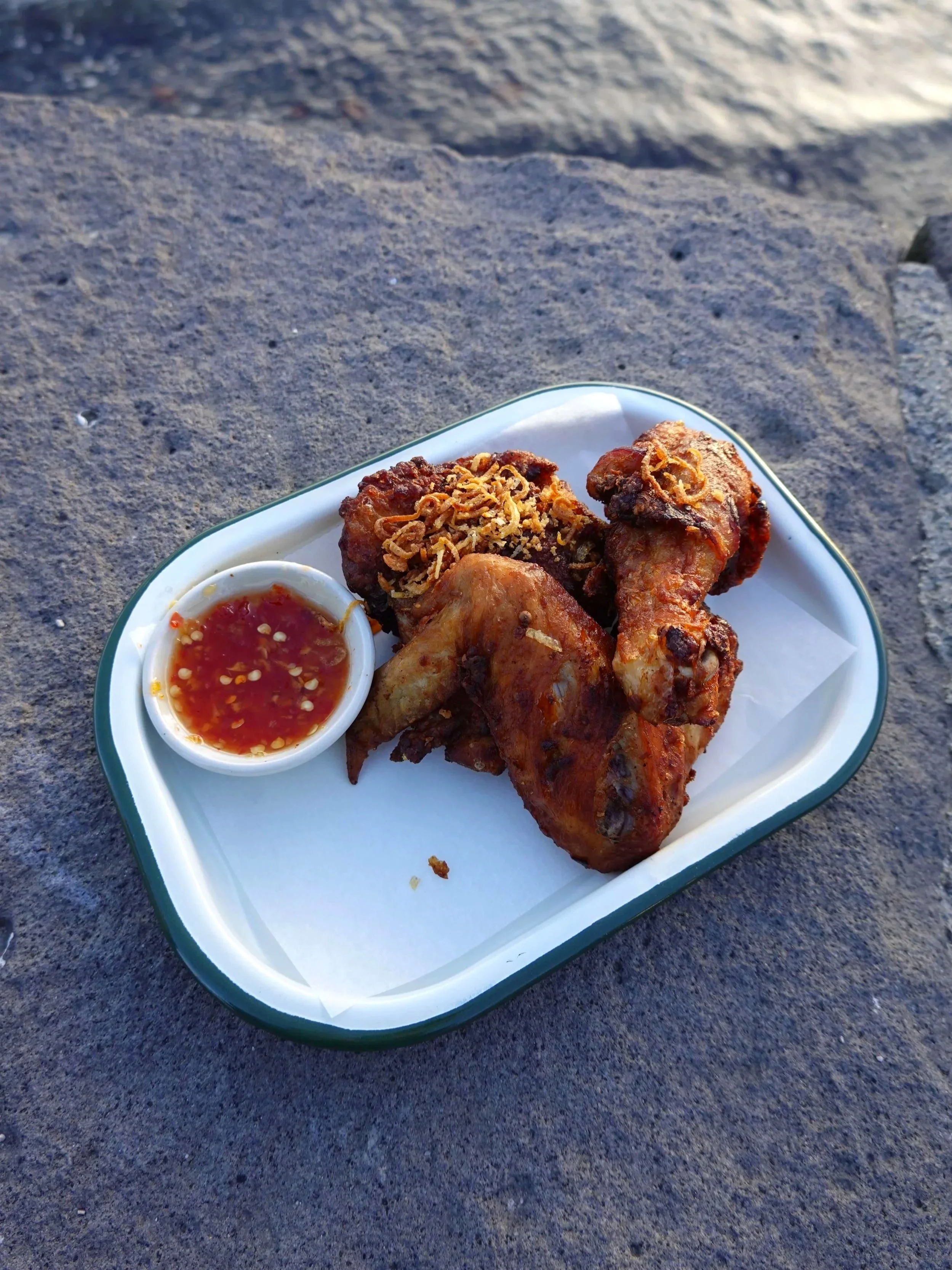 Fried chicken drumsticks with a side of house made sweet chilli dipping sauce, served on a white tray.