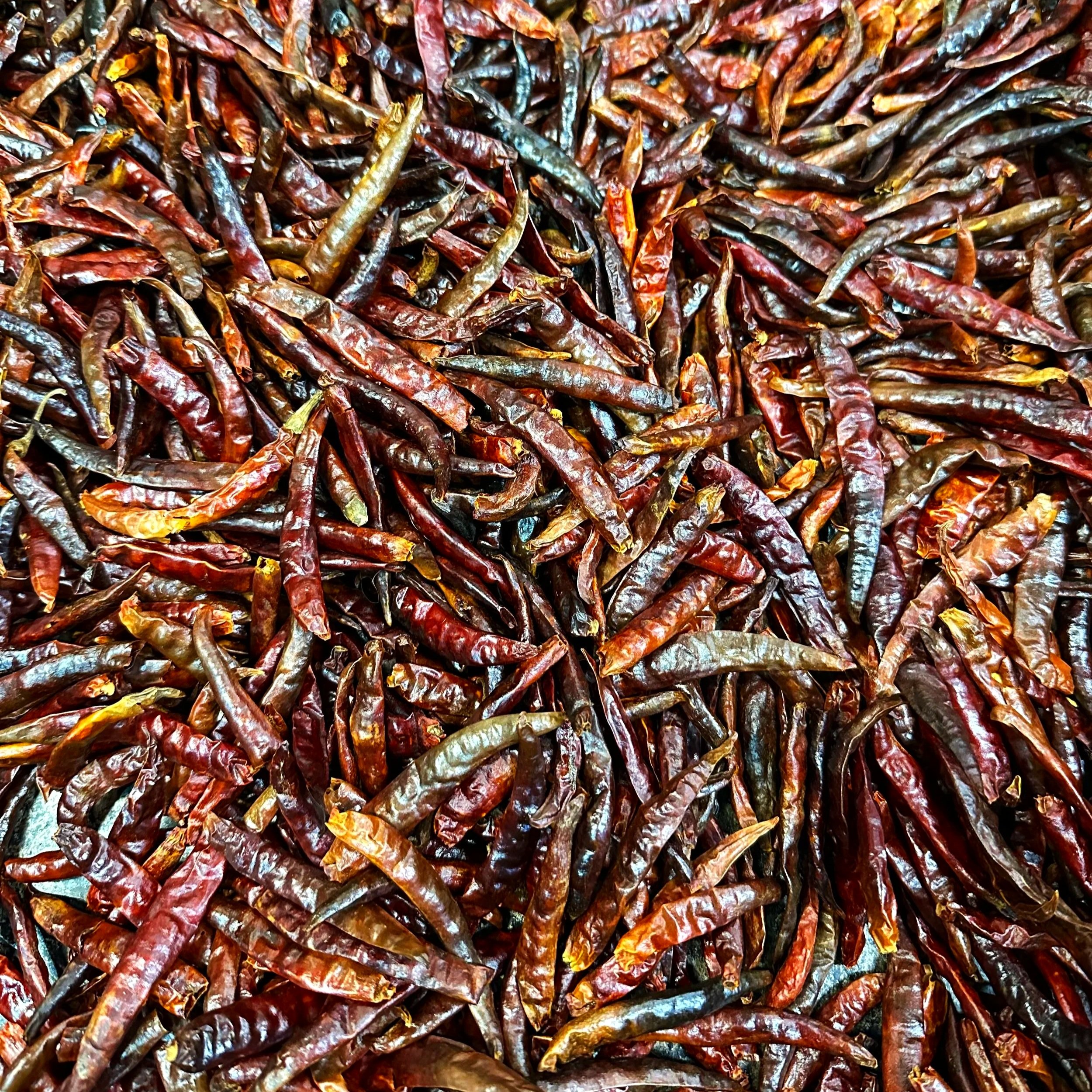 A close-up of numerous dried red chili peppers scattered on a surface.