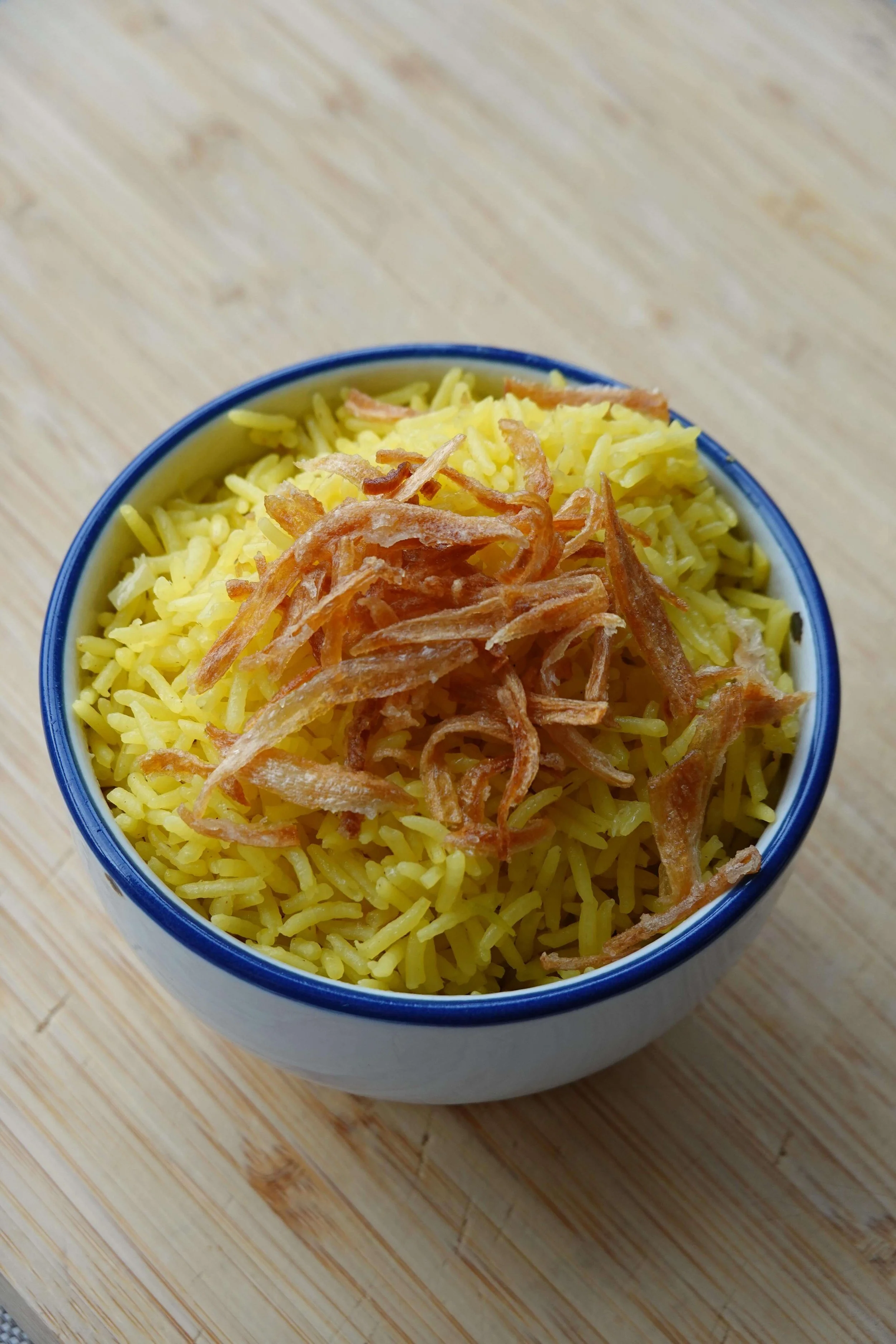 A bowl of fried rice topped with shredded crispy pork on a wooden surface.