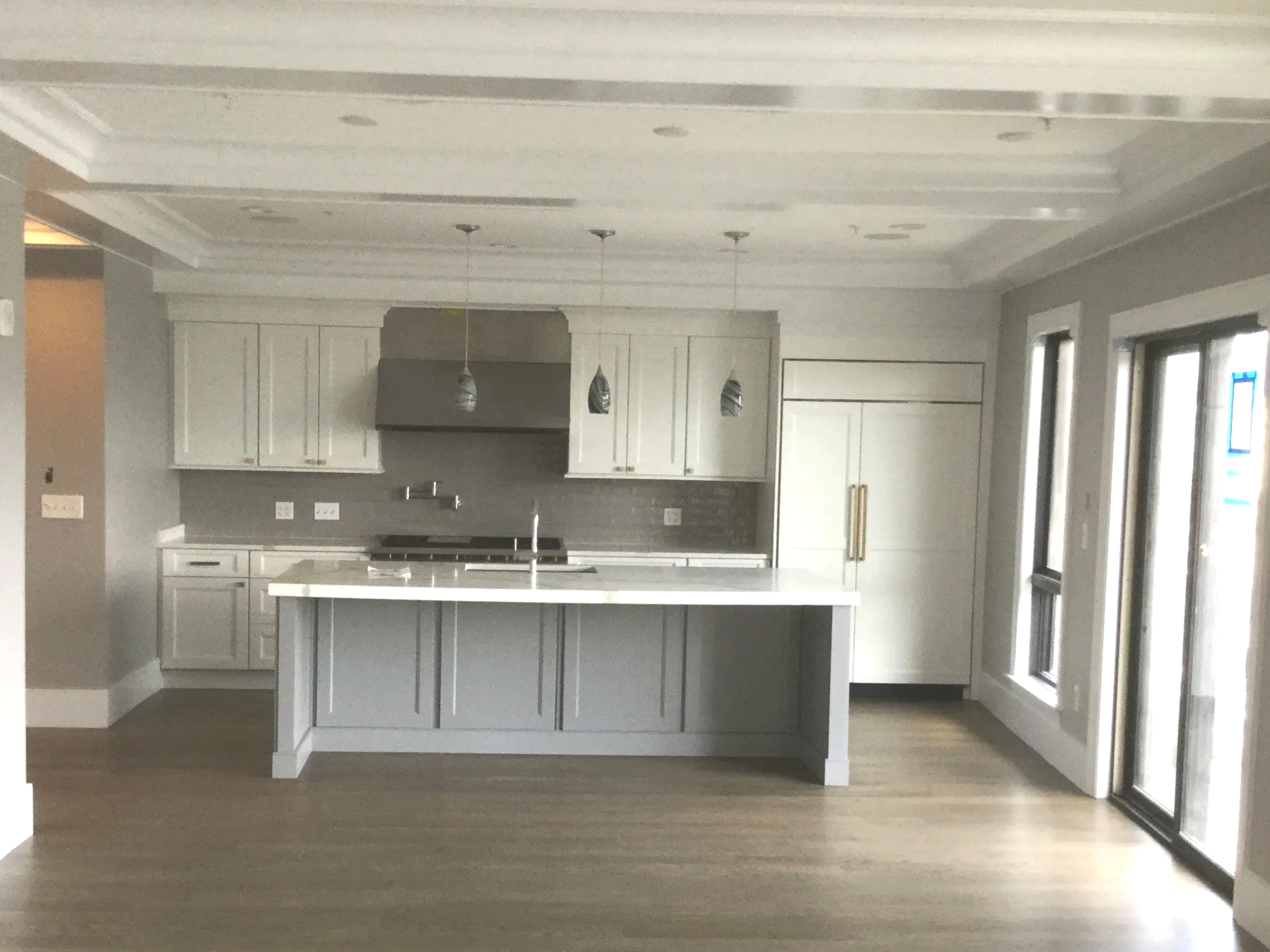 Modern white kitchen with island, pendant lights, and large windows. New construction, minimalist design.