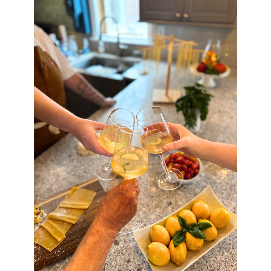 Family and friends raising glasses around the kitchen table after making fresh pasta together