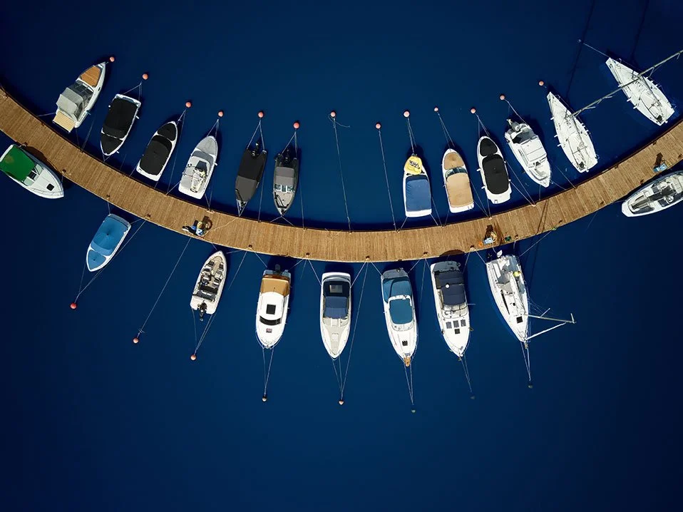 Immagine aerea di un molo di legno con barche attraccate, circondata da acque blu.