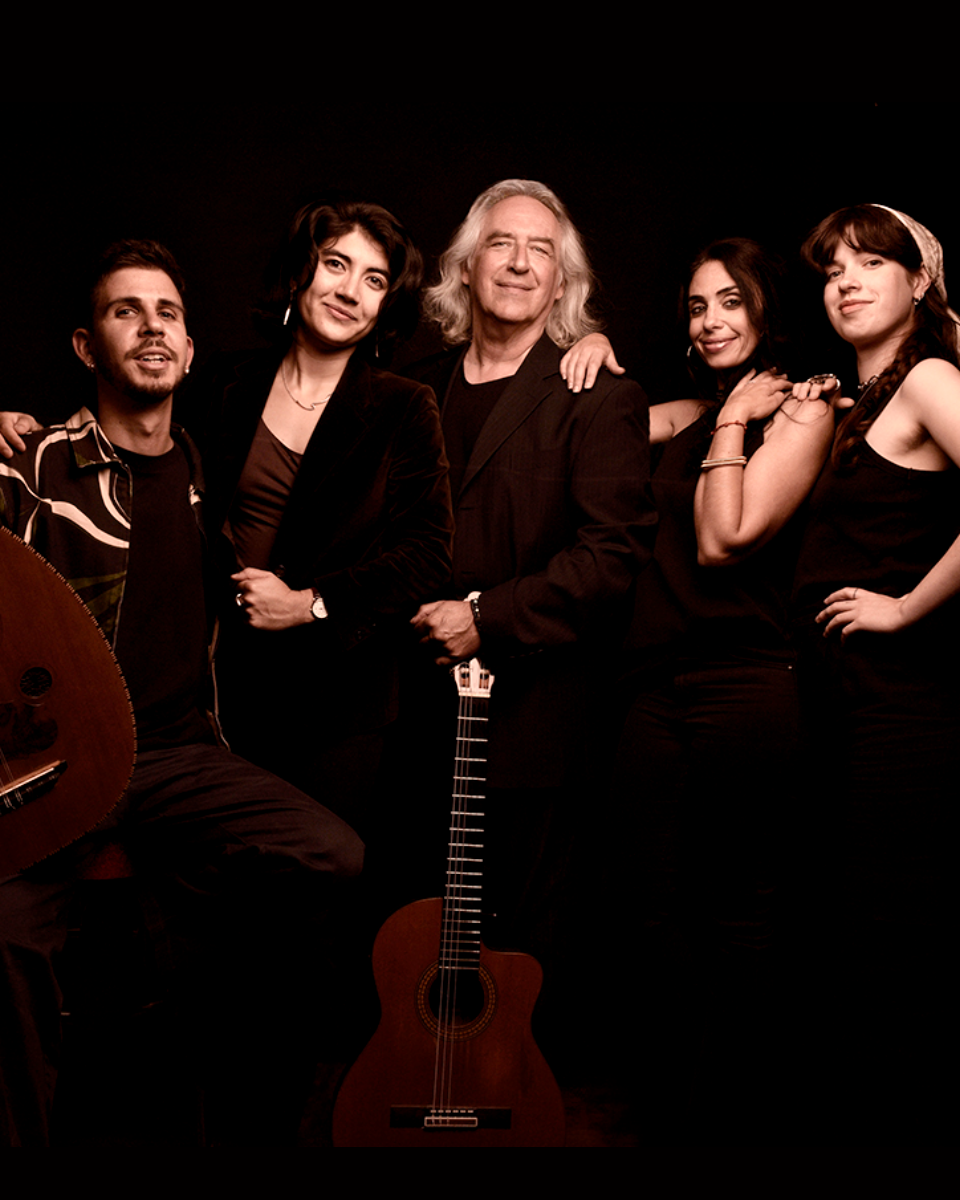 Groupe de cinq personnes posant avec deux guitares acoustiques contre un fond noir.