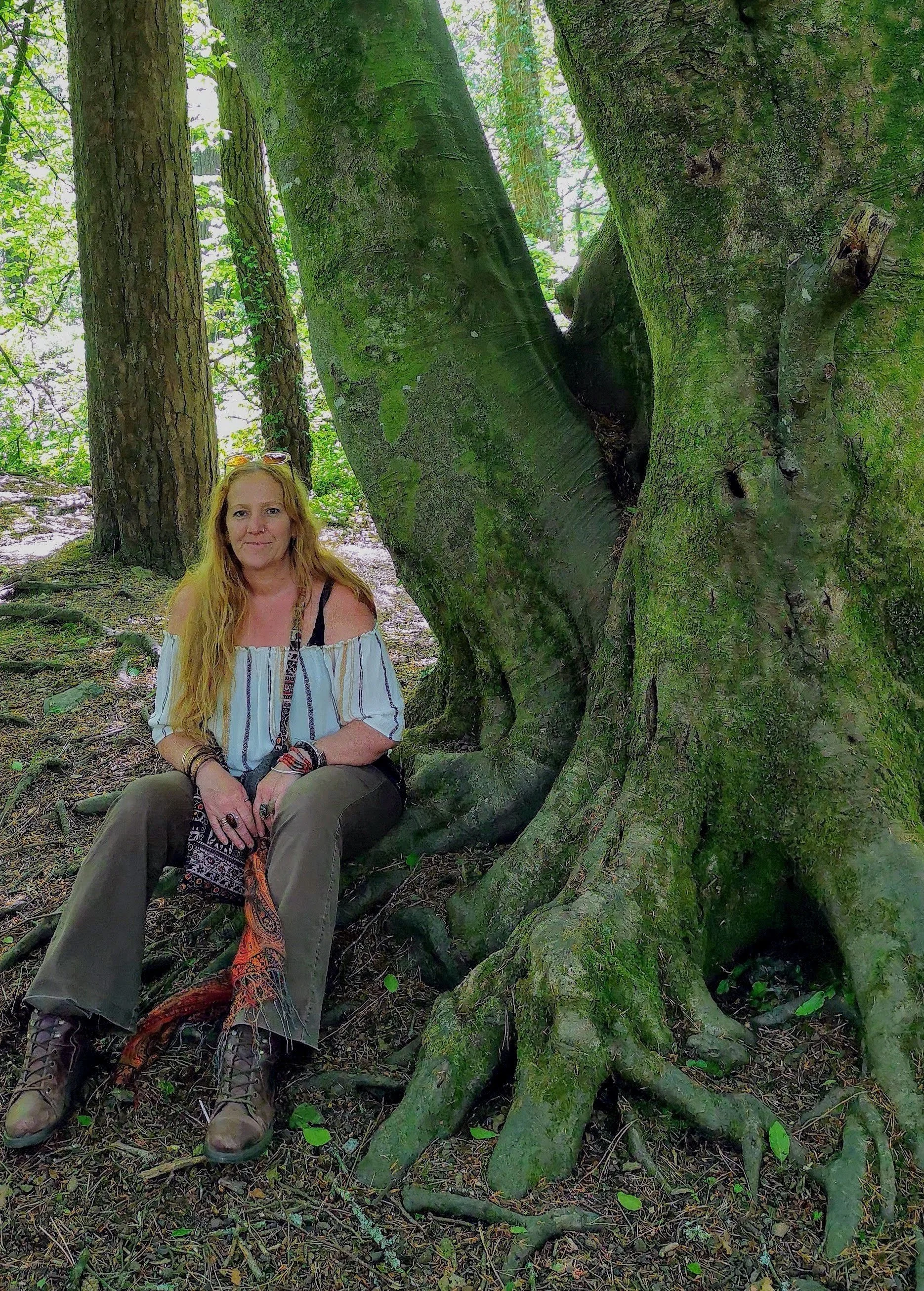 Cornwall artist Shelly Cook sitting beside an ancient moss covered tree in woodland.