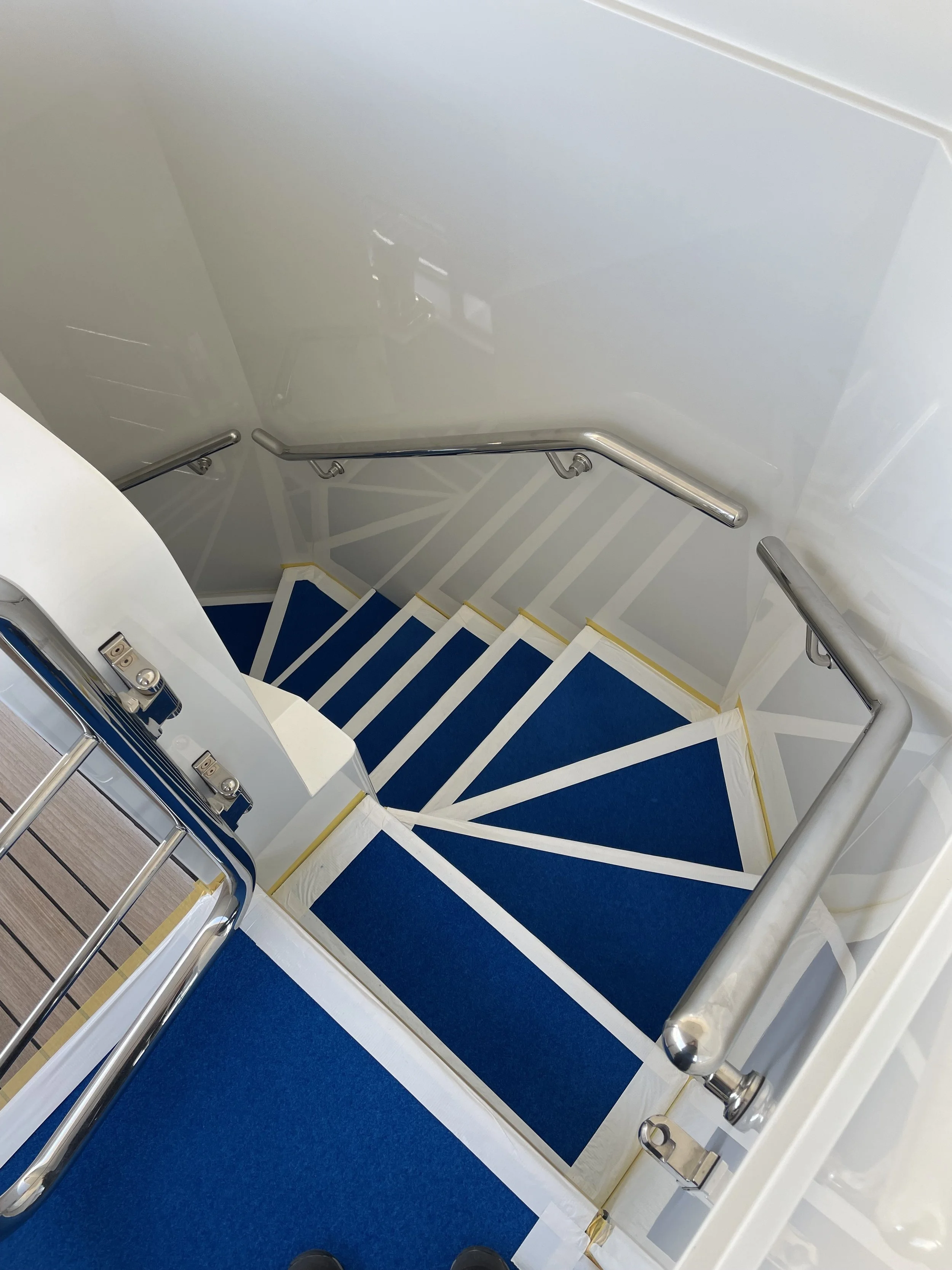 Escalier extérieur de navire avec rampes en métal et moquette bleu de chantier, vue du haut.